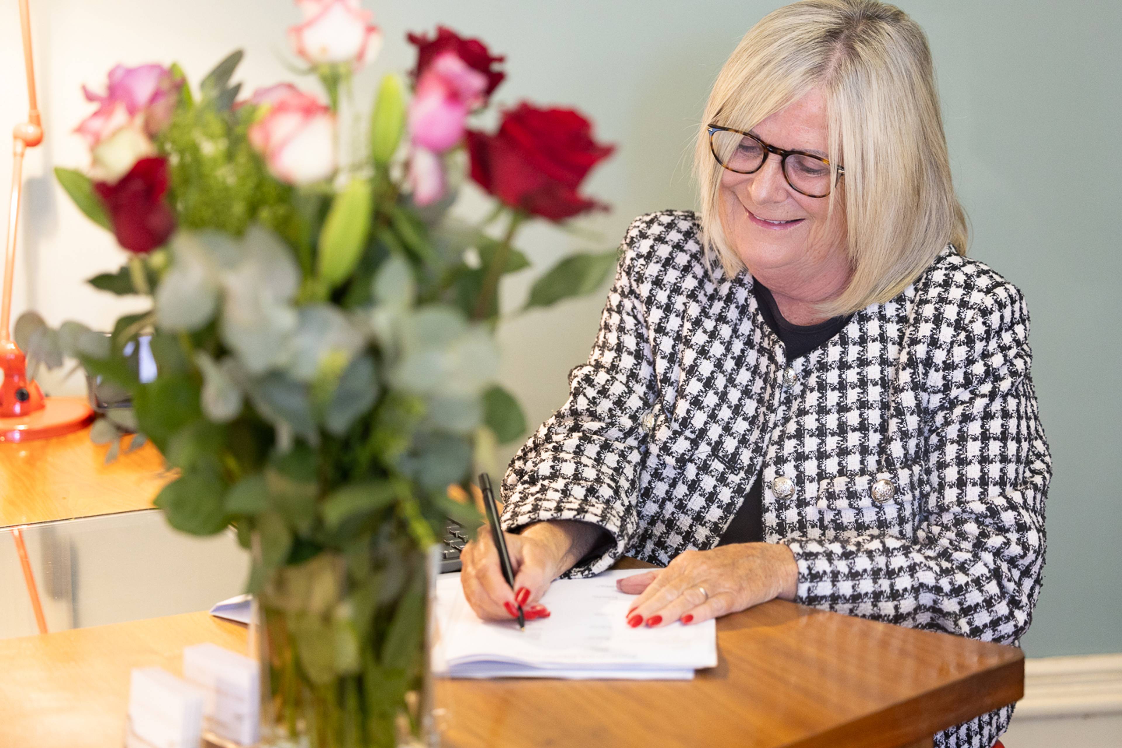 Receptionist at Pontcanna Dental Care writing in a note book at a wooden reception desk next to pink and red flowers in a vase