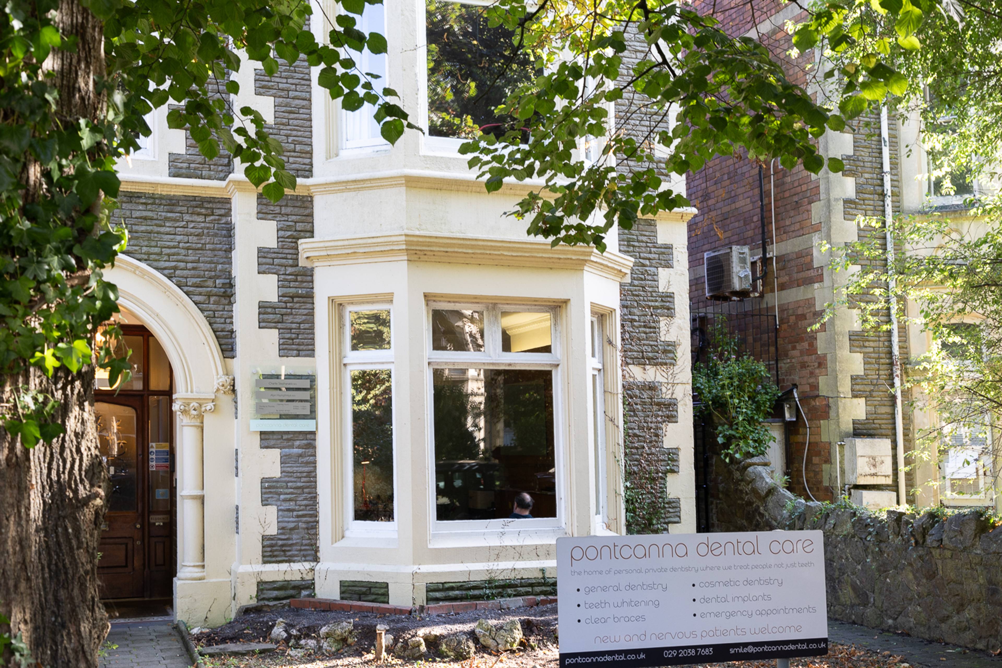 Outside Pontcanna dental care front of building and brand signage in garden with large overlooking tree
