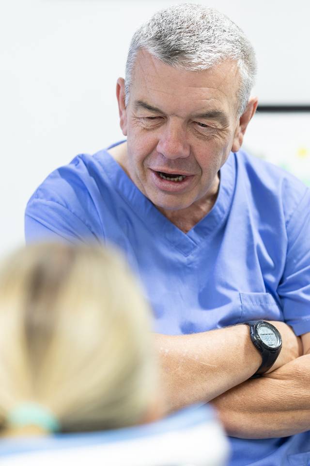 Dentist with arms crossed listening to patient in the dental chair in front