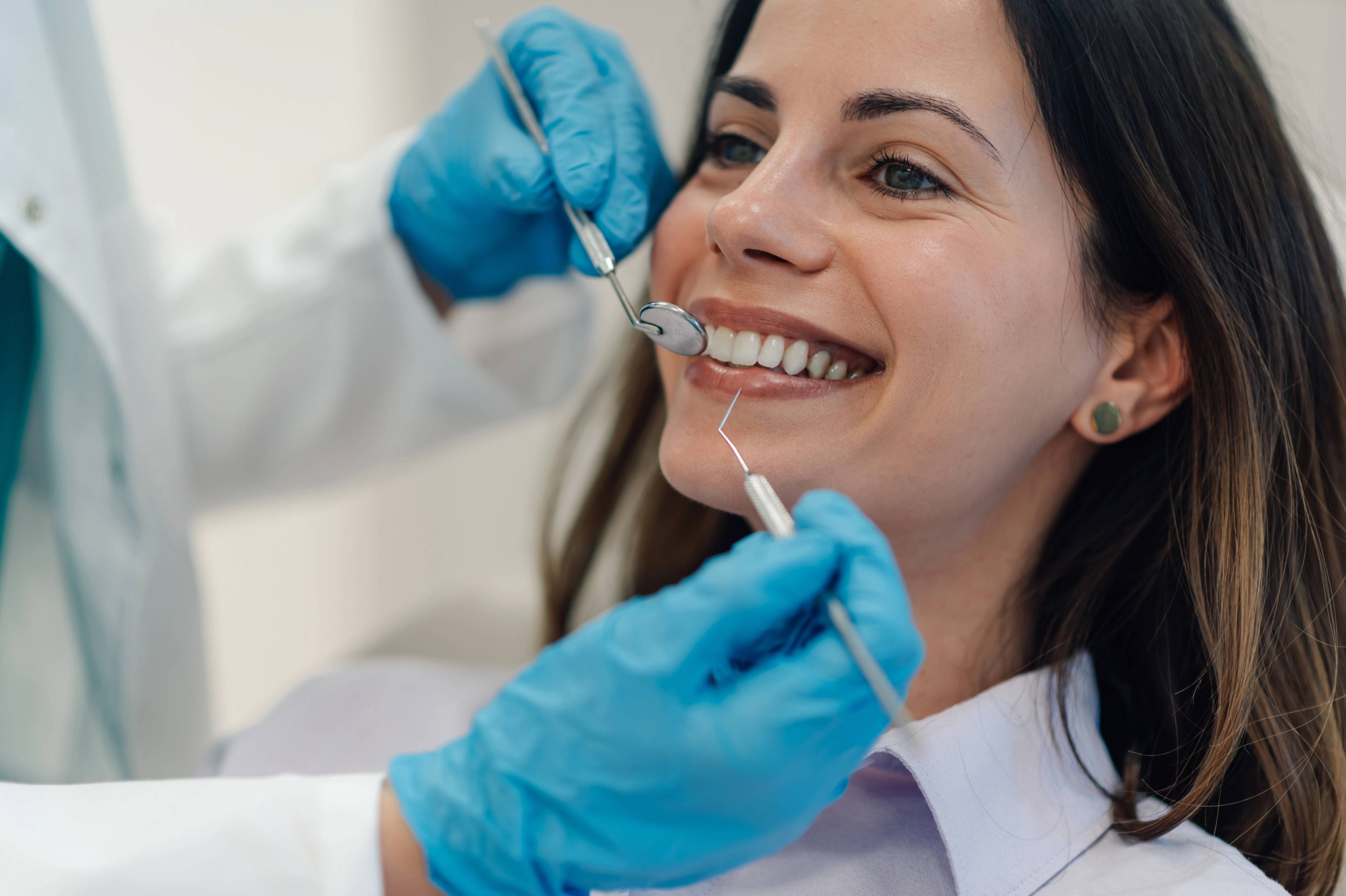 Smiling young female patient with dentist holding tools and wearing blue gloves