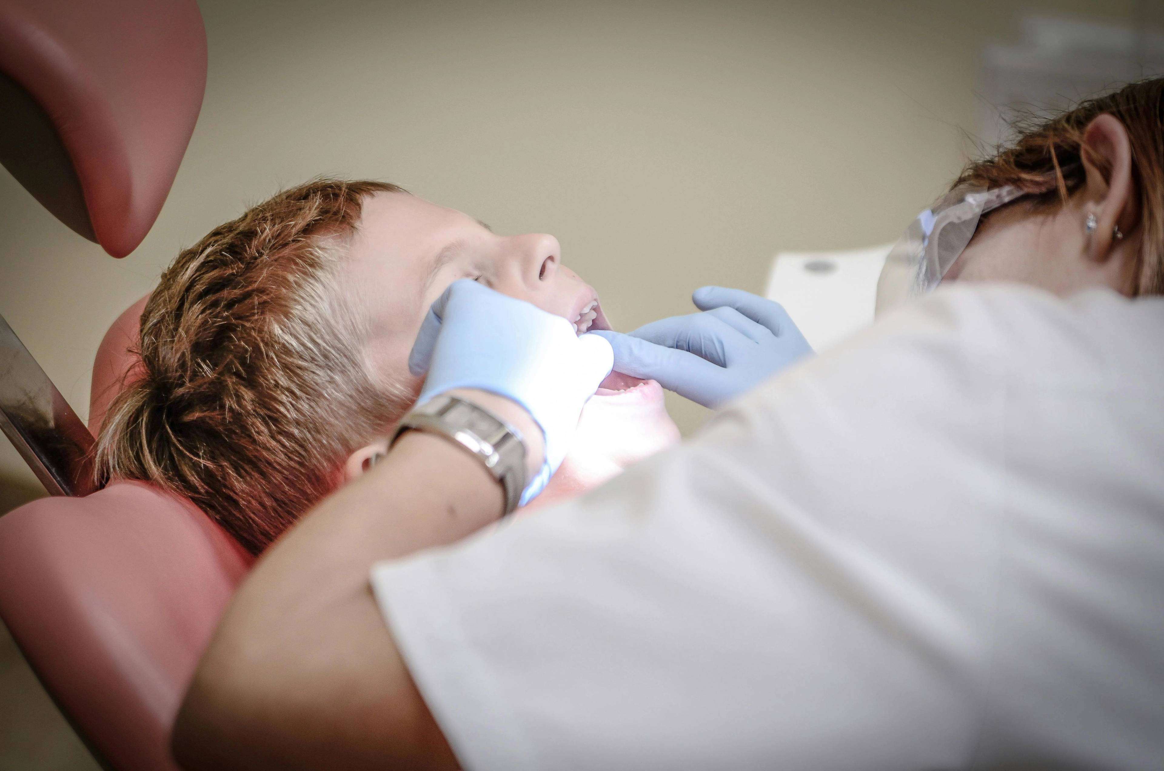 child patient lying in dental chair having check up from dentist wearing blue gloves 