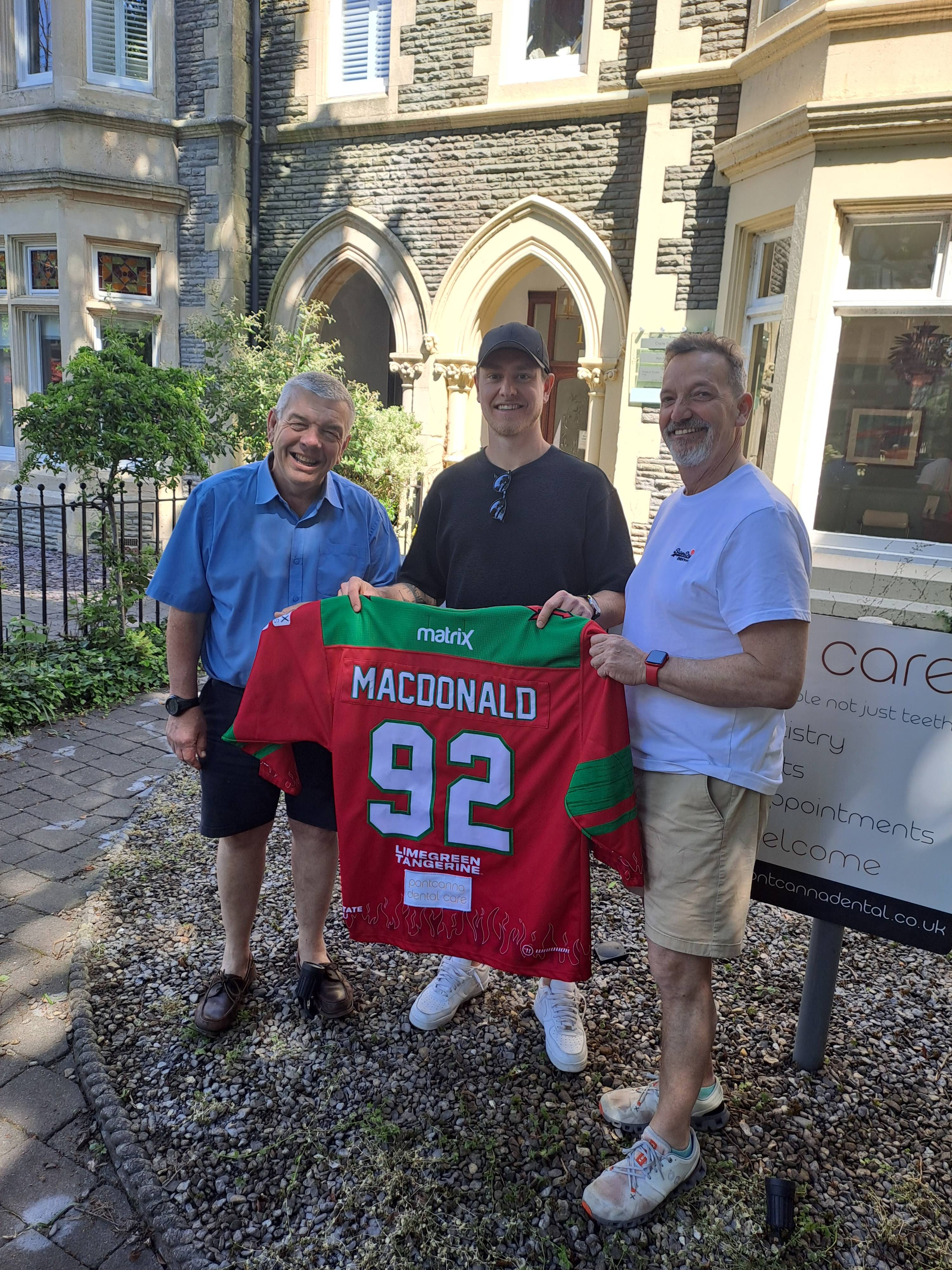 Pontcanna Dental Care dentists smiling with Cardiff Devils ice hockey player in front of the practice holding his jersey saying MacDonald