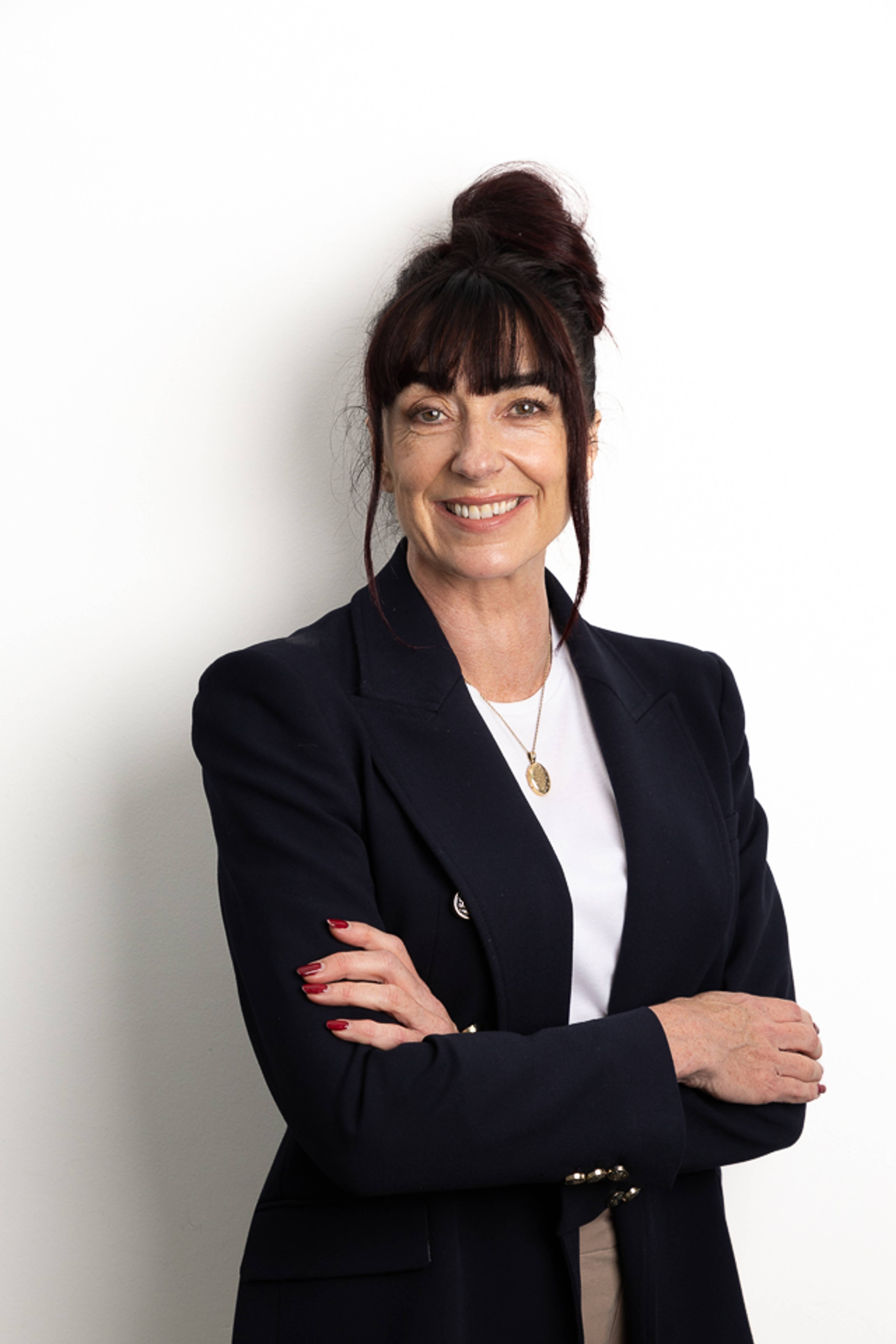 Receptionist at Pontcanna Dental Care smiling at camera against white wall wearing smart blazer