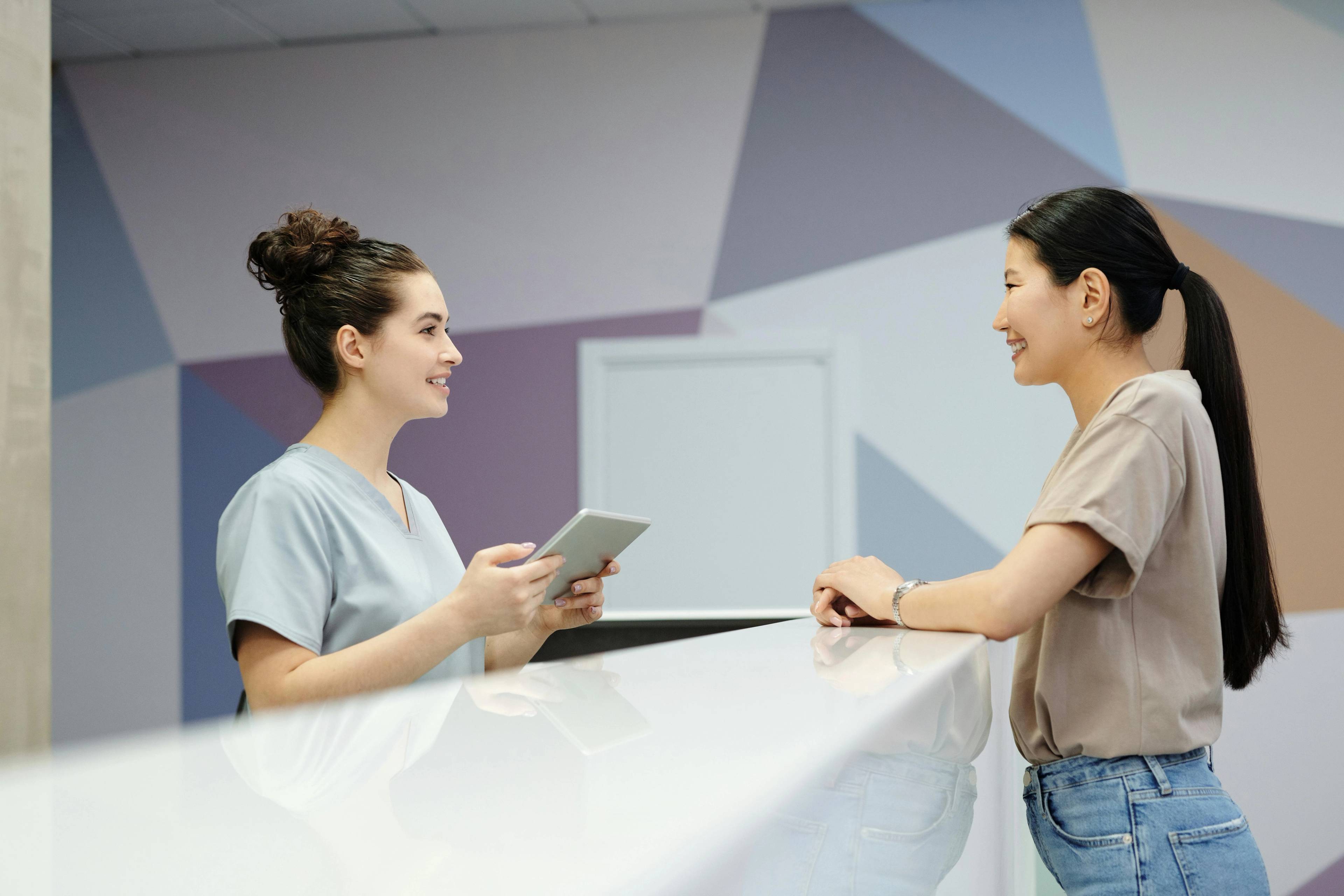patient at reception desk talking to dental nurse holding ipad with finance application