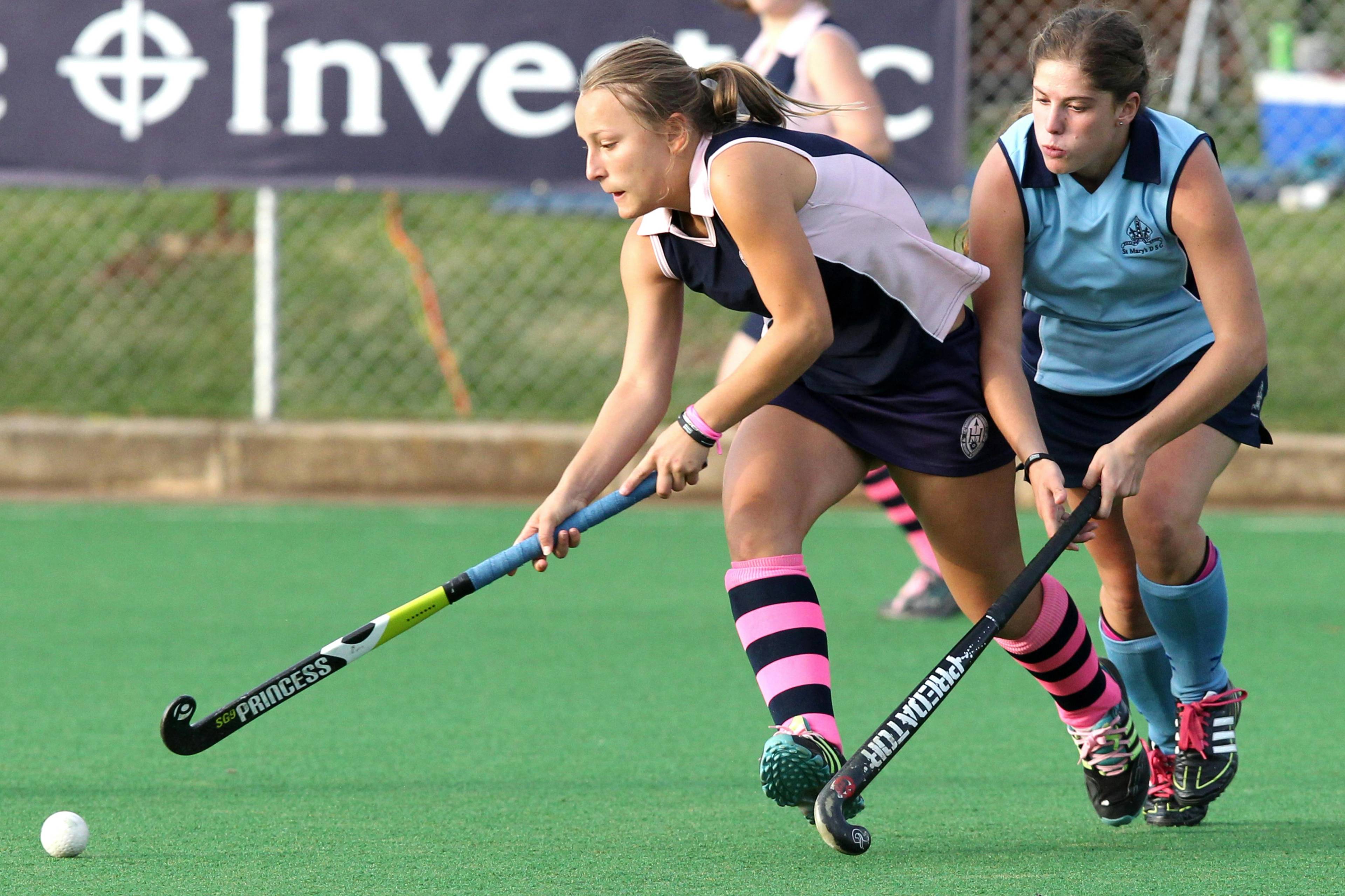 two female hockey players running after the ball with their sticks whilst wearing protective sport guards