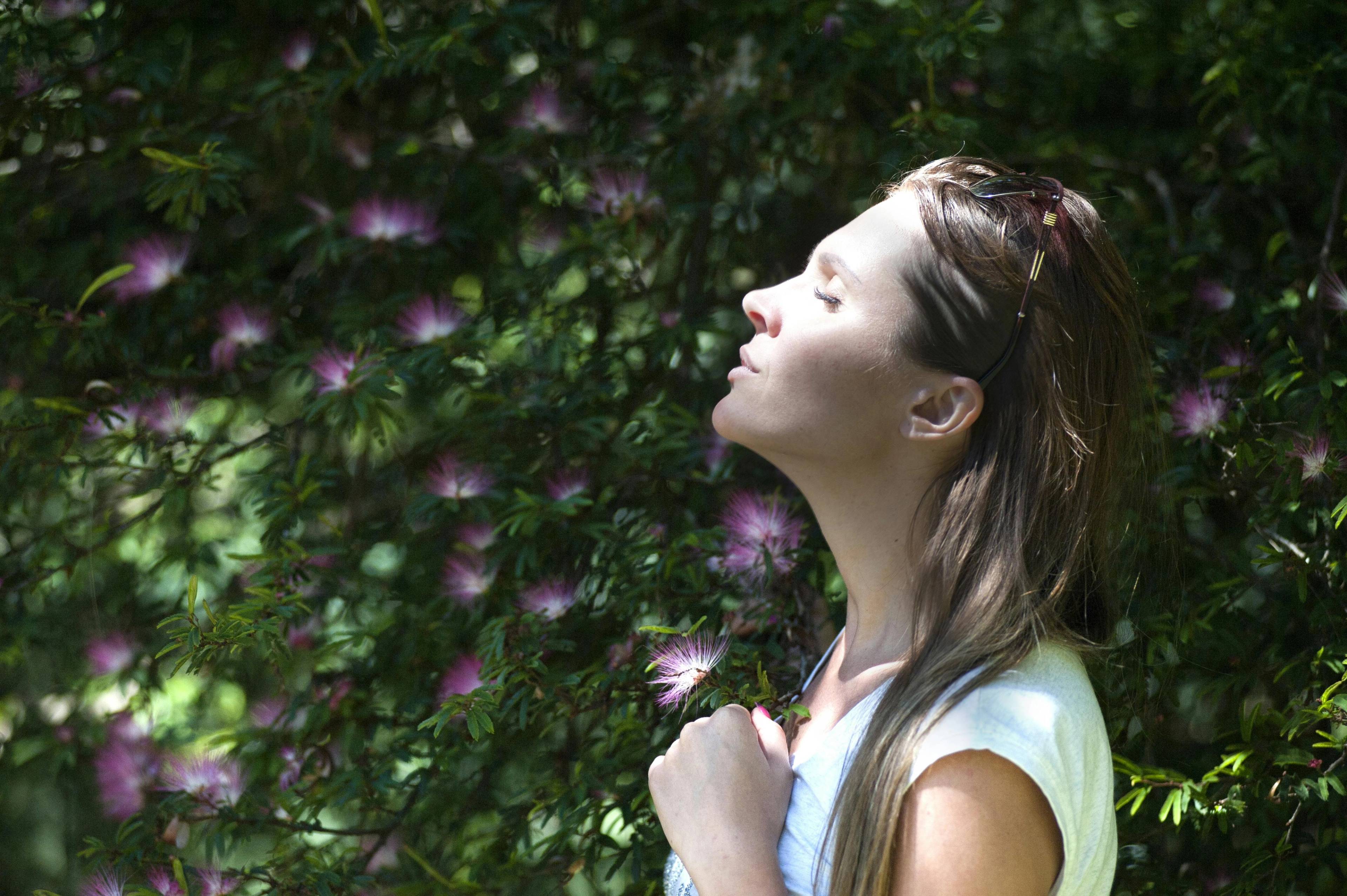 female wearing white t-shirt standing in flower garden and looking up towards sun 