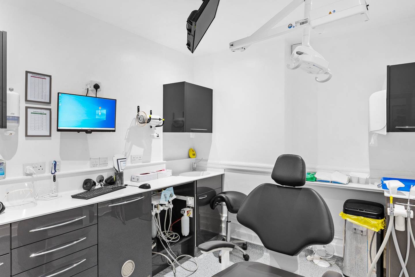 inside dental surgery featuring black and white interior cupboards, hygienic waste disposal and patient chair with screen on the wall behind