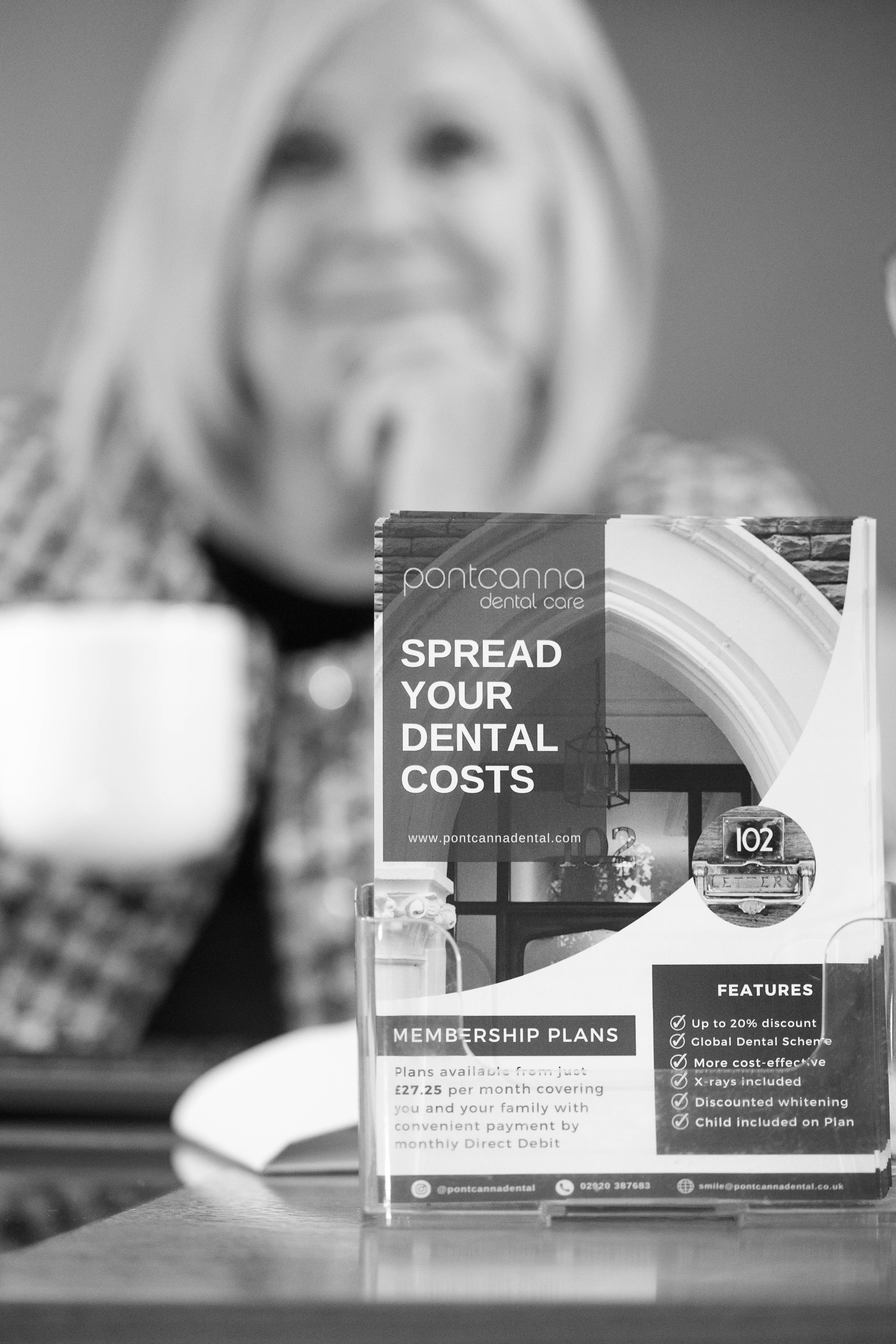 Black and white photo of dental pricing information leaflet in display stand on reception desk with receptionist in background
