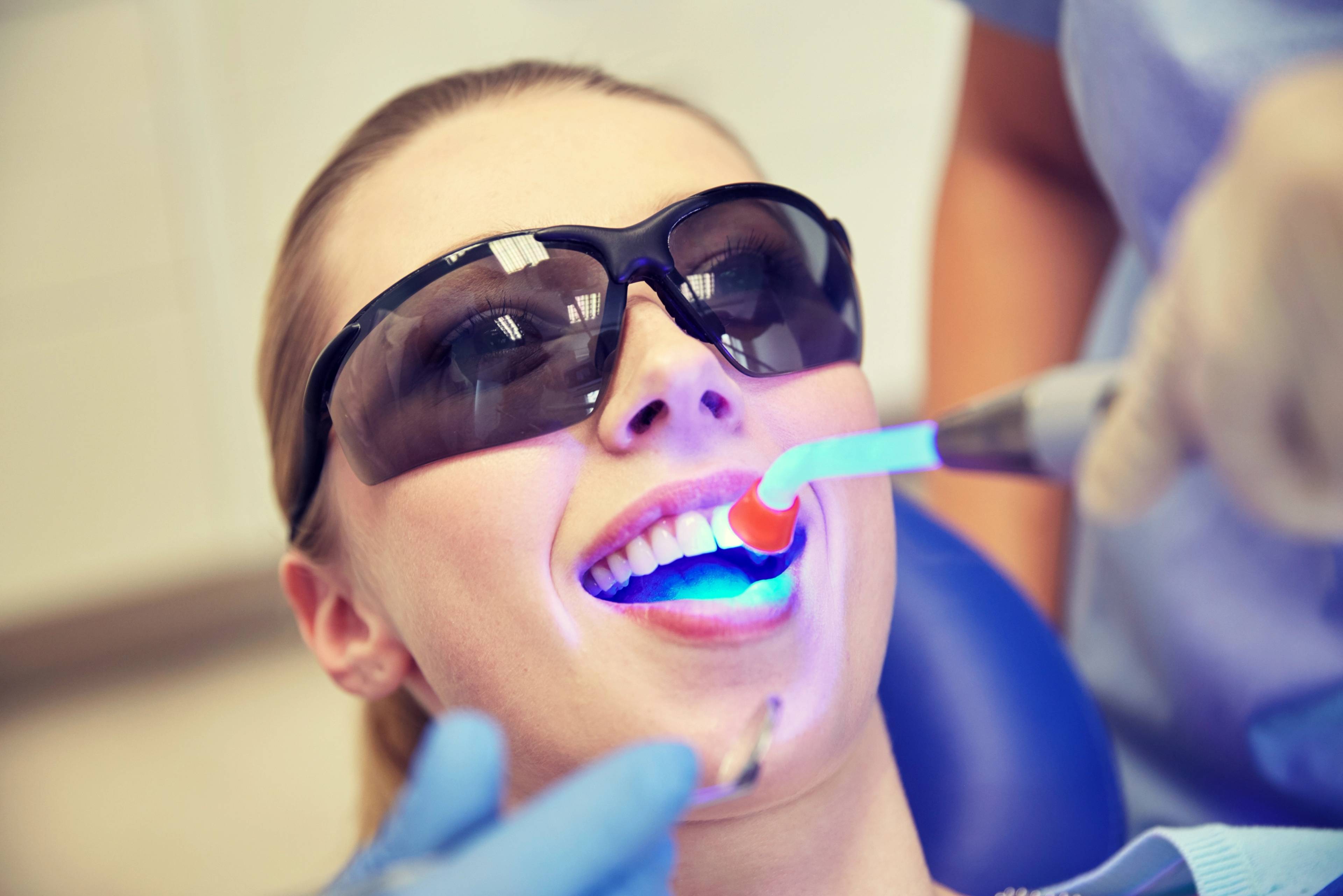 Patient wearing protective glass, lying back on dental chair whilst curing light is held over teeth