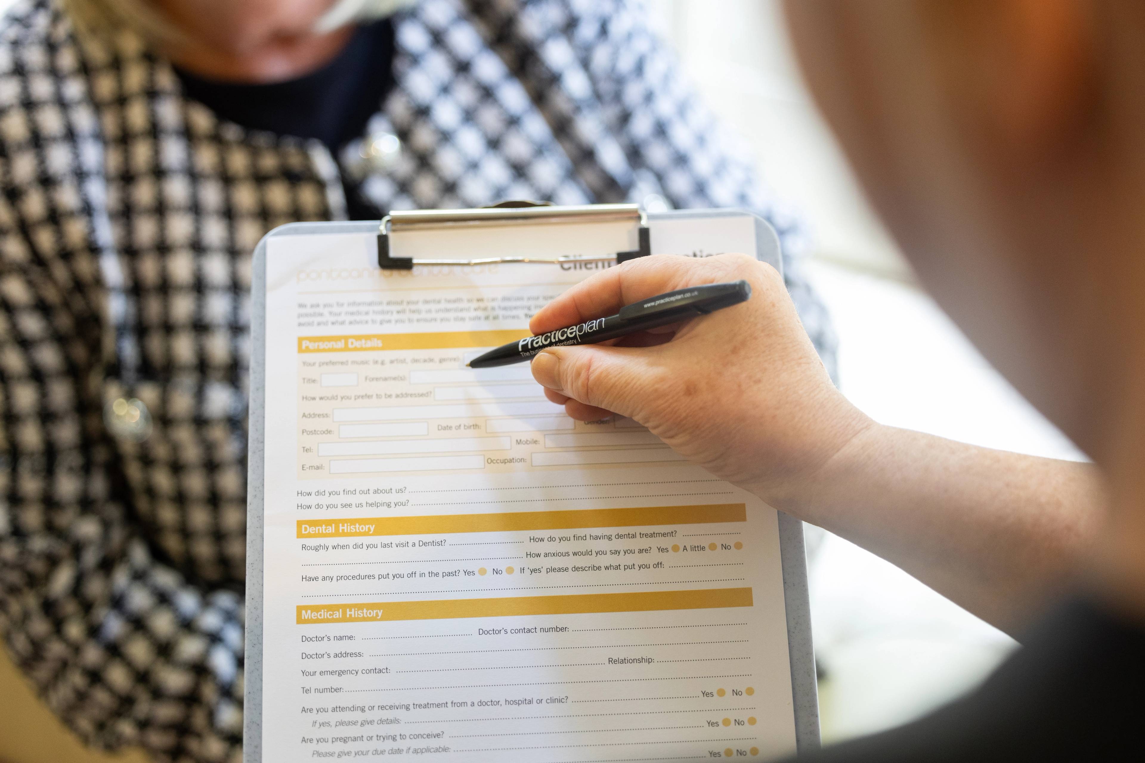 close up of patient holding pen and patient information form on clipboard