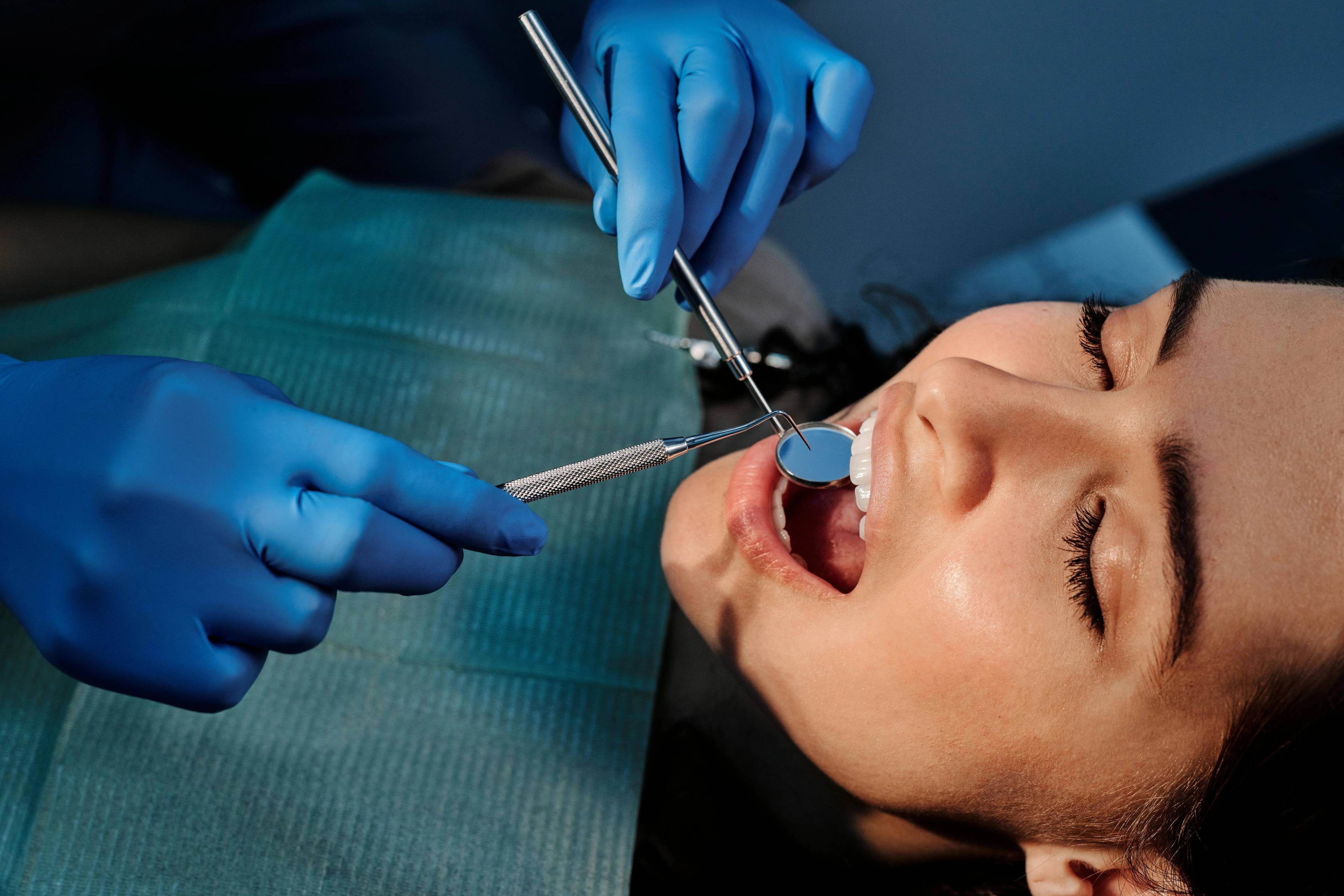 Dentist performing routine dental check up on young female patient sat in the dental chair