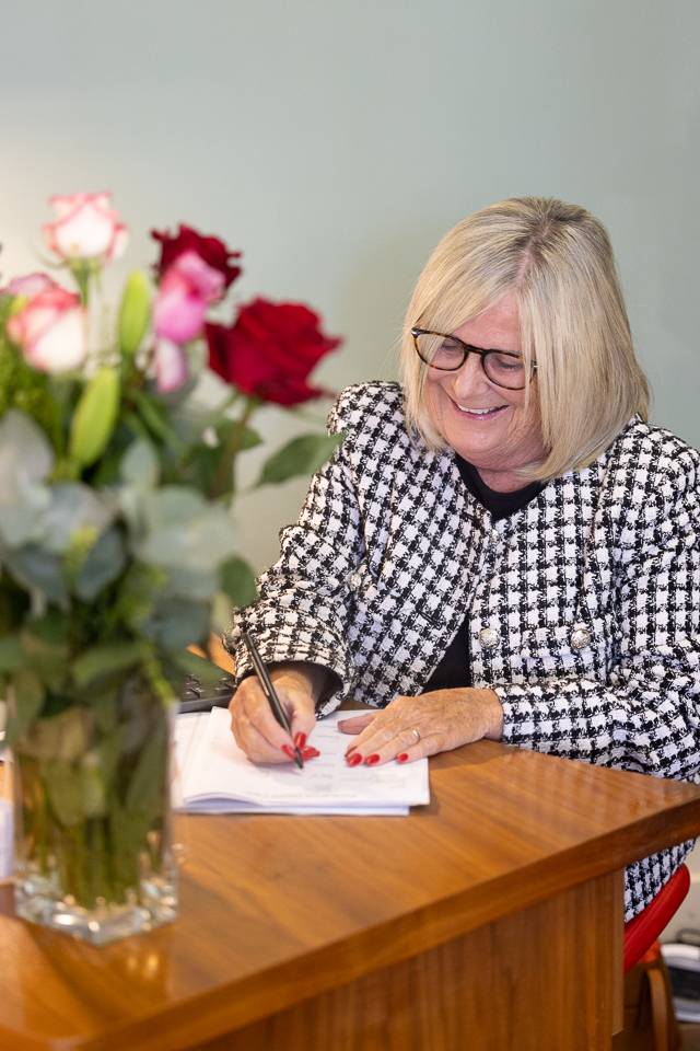female receptionist writing at desk with vase of brightly coloured flowers
