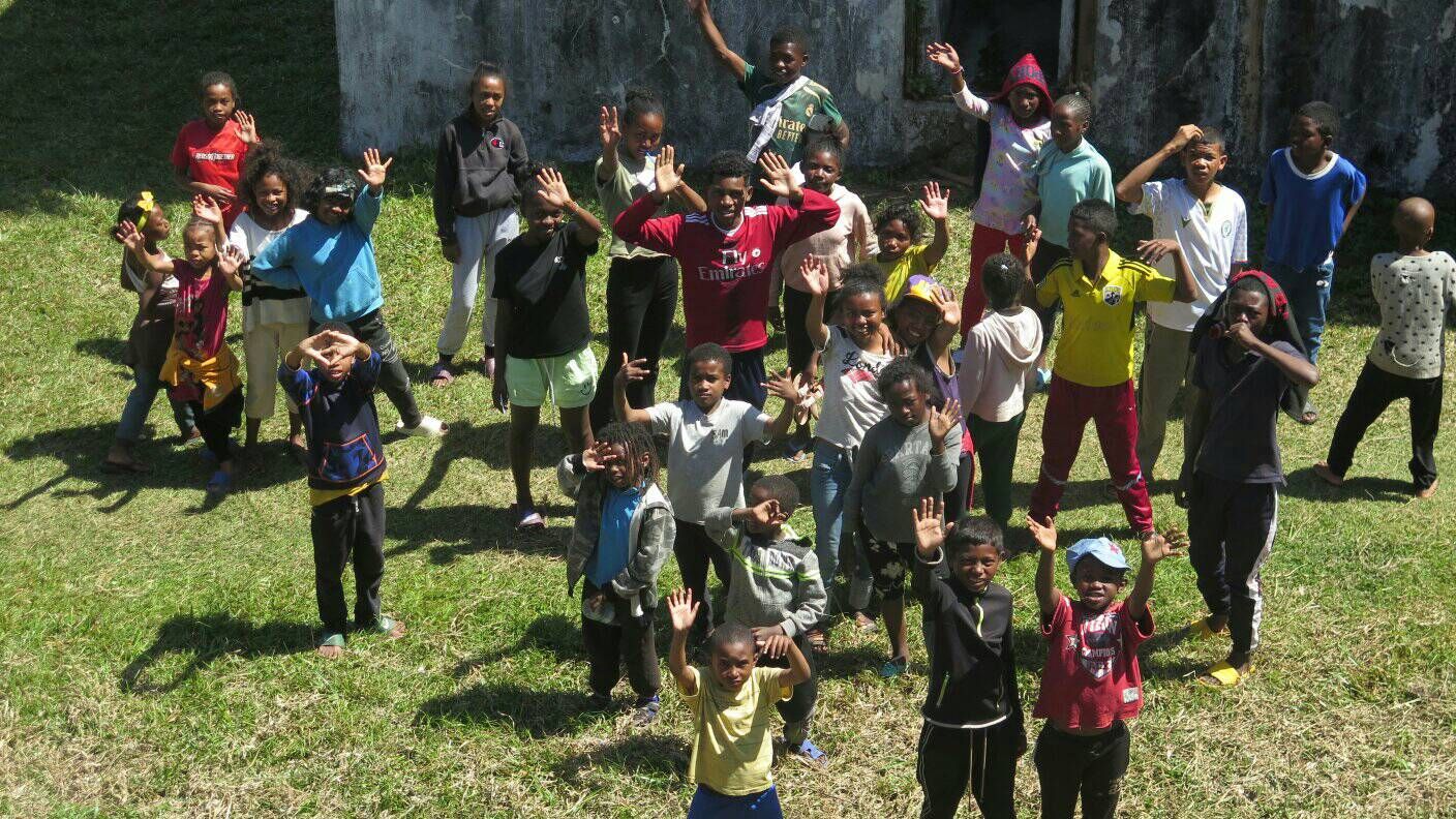 Kinder und Jugendliche winken auf einer Wiese in die Kamera.