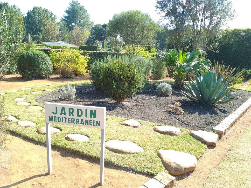 Ein gepflegter Garten mit dem Schild „Jardin Méditerranéen“ und Zierpflanzen.