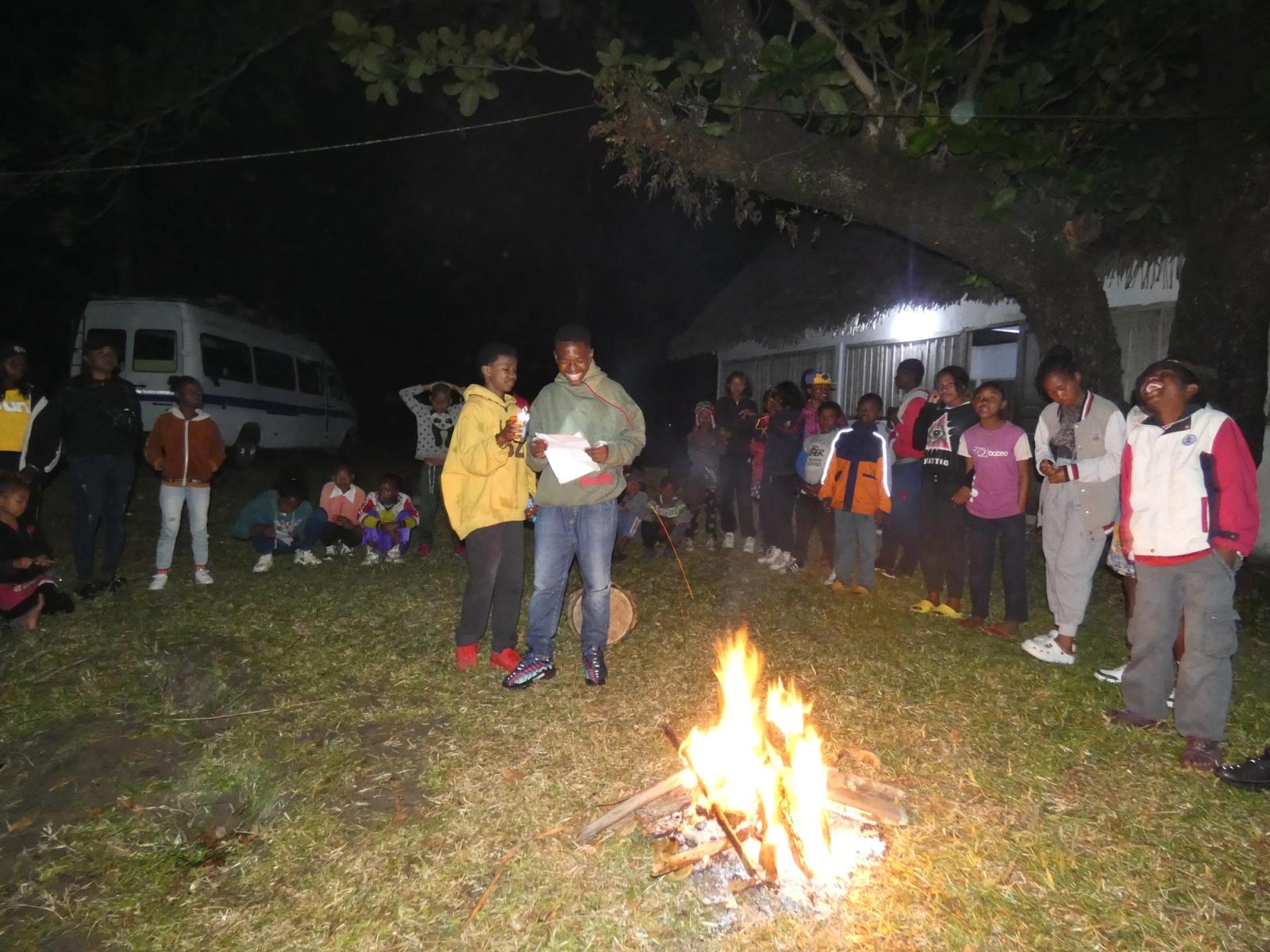 Kinder und Jugendliche stehen nachts um ein Lagerfeuer.