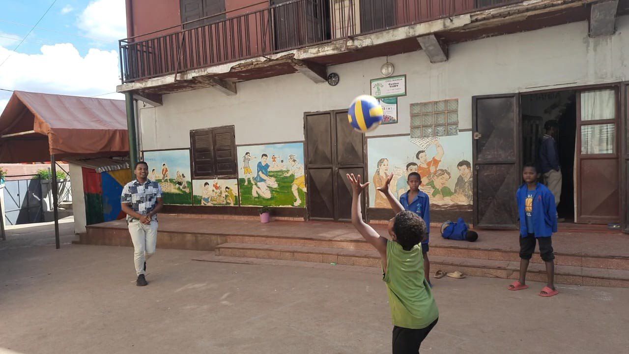 Kinder spielen Volleyball in einem Hof; der Ball fliegt über der Gruppe.