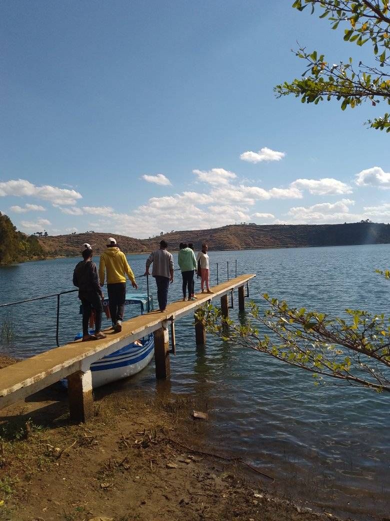 Jugendliche gehen über einen Steg zu einem Boot am See.