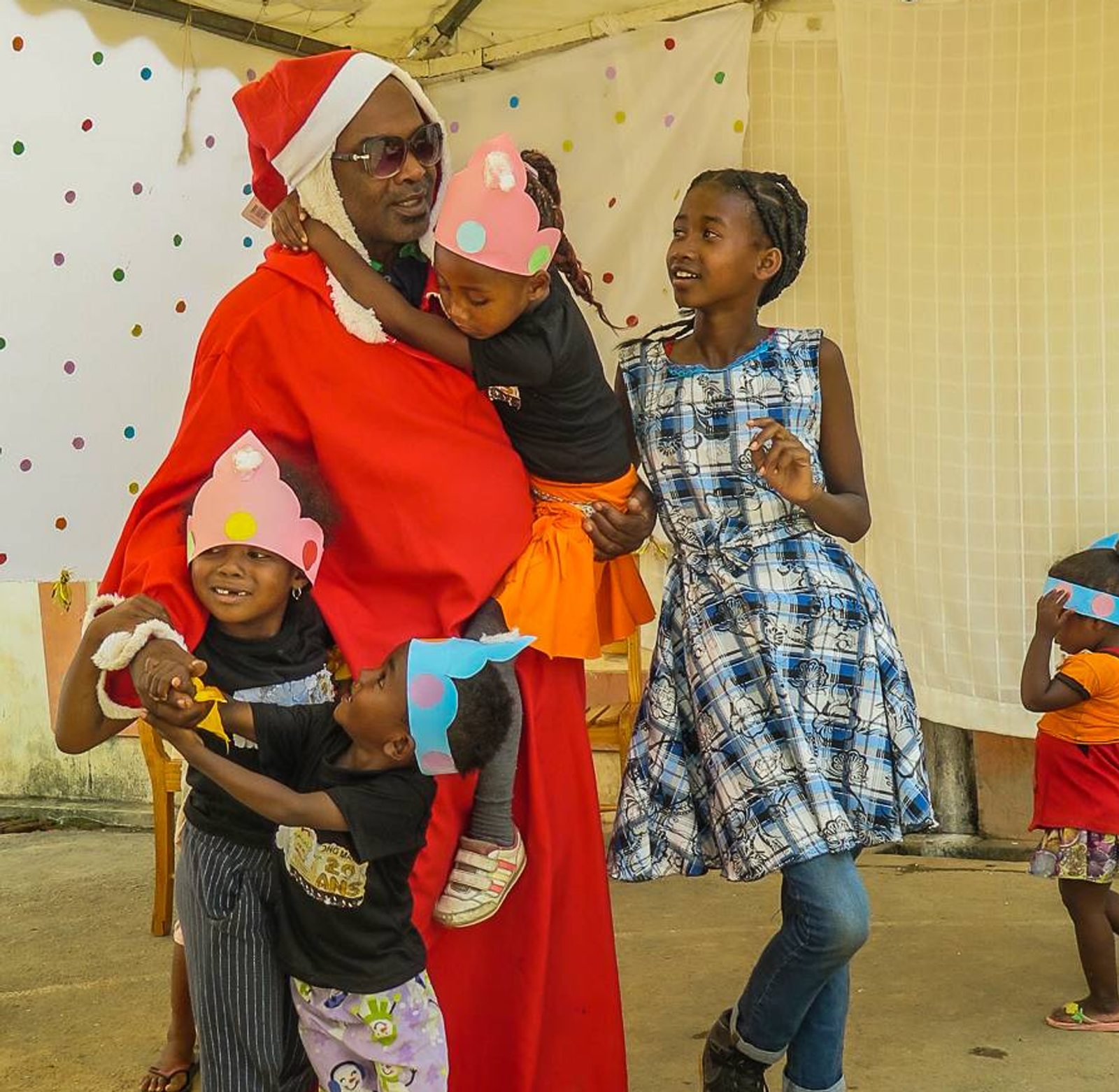 Ein Erwachsener im Weihnachtsmannkostüm feiert mit Kindern in bunten Kostümen.