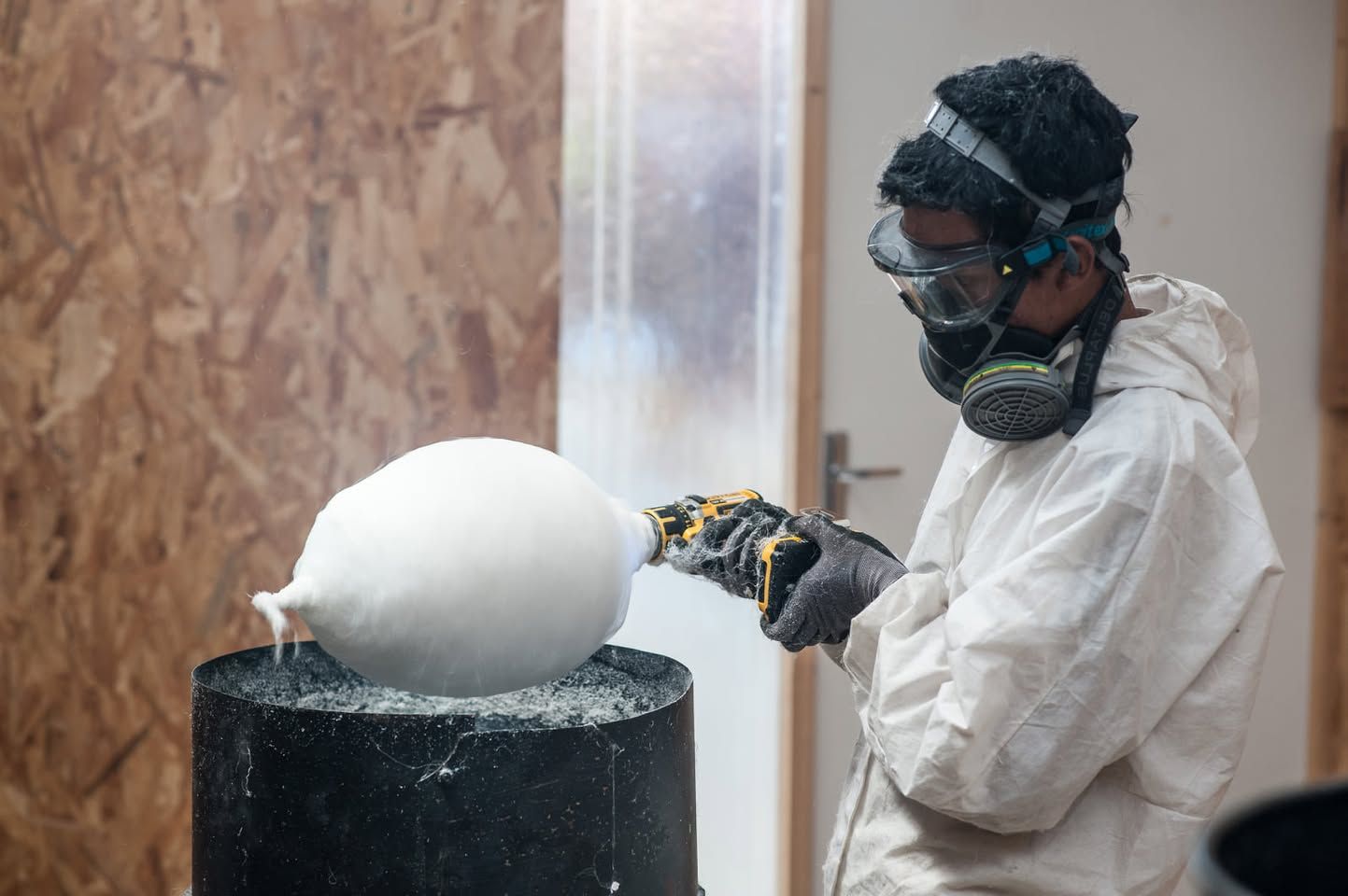 Eine Person in Schutzkleidung arbeitet mit einem Werkzeug an einer weißen Skulptur.