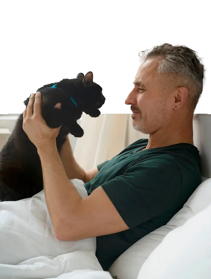 Un hombre tumbado en la cama con un gato negro en su pecho