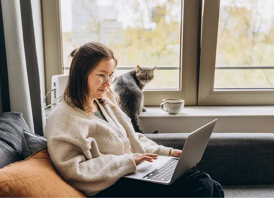 Persona trabajando con un portátil junto a un gato en la ventana