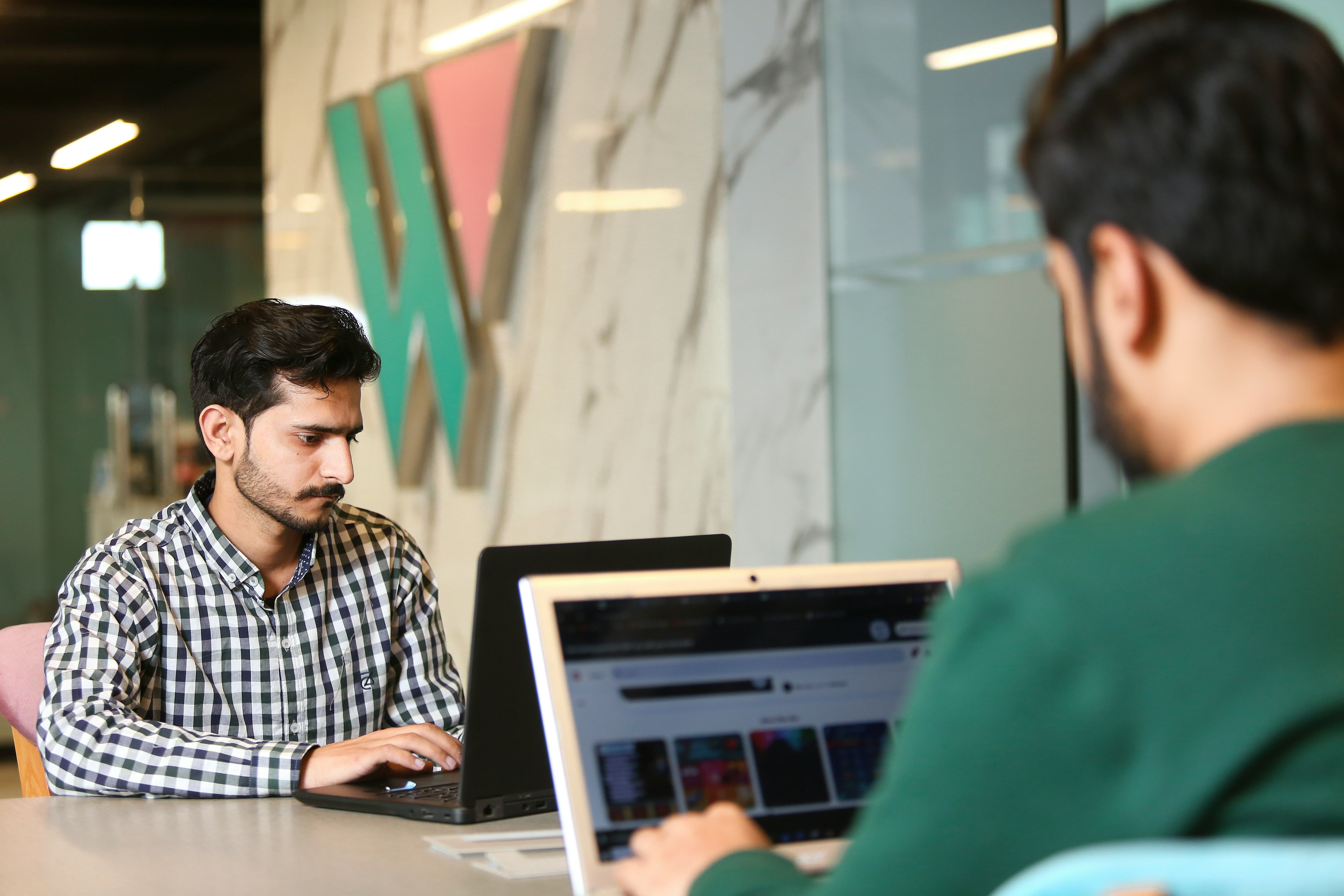Office working photo featuring two men at laptops and a generic company logo in the background