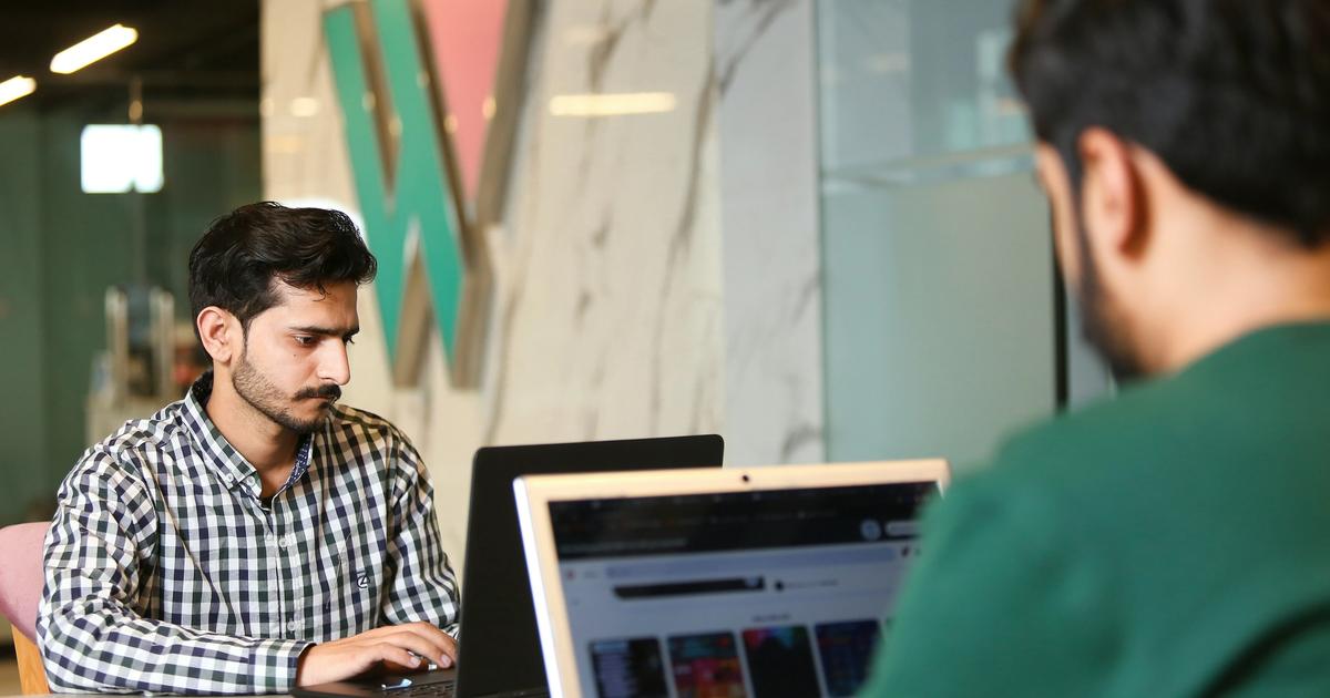 Office working photo featuring two men at laptops and a generic company logo in the background