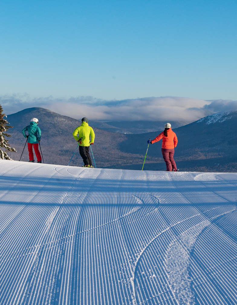 Three skiers overlooking a scenic mountain at Sunday River