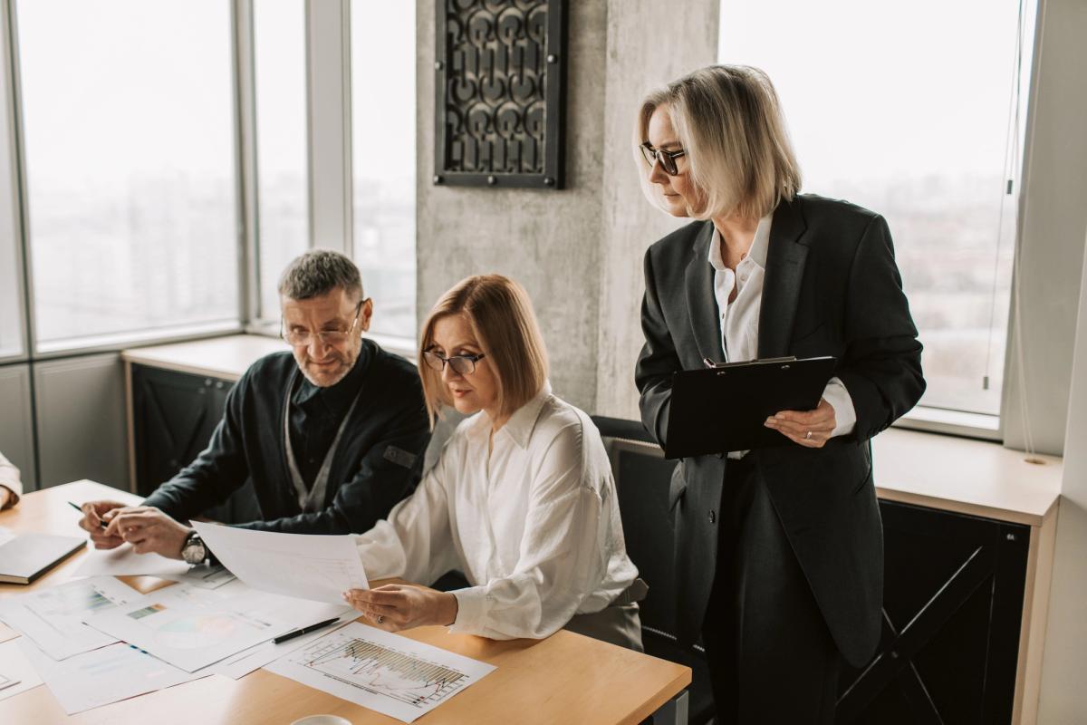 Three professionals reviewing printed financial documents and charts together at a desk