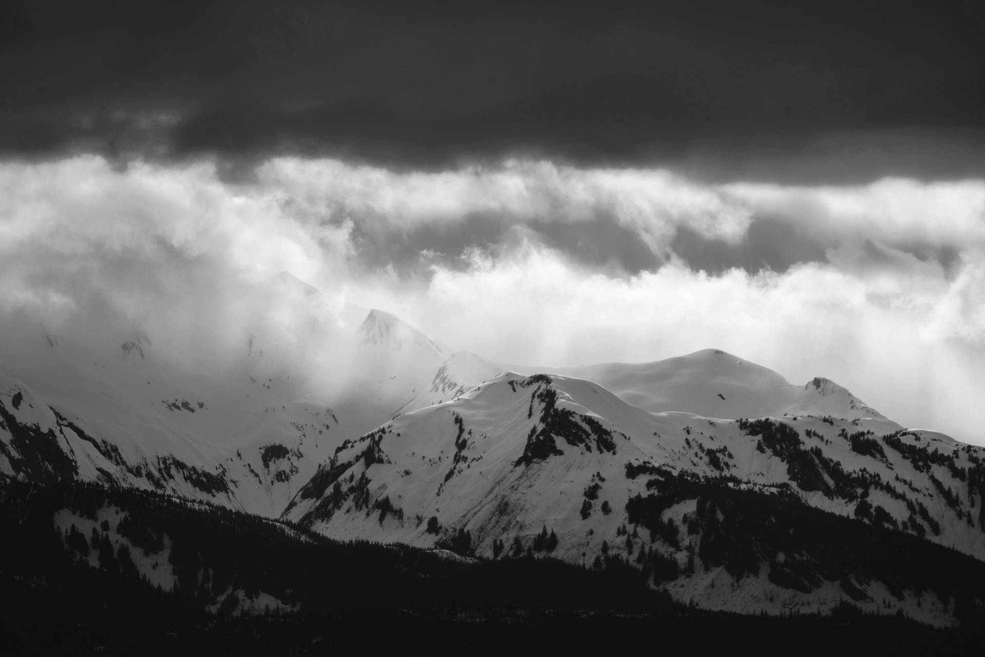 Snow-covered mountain peaks under dramatic dark clouds and swirling mist