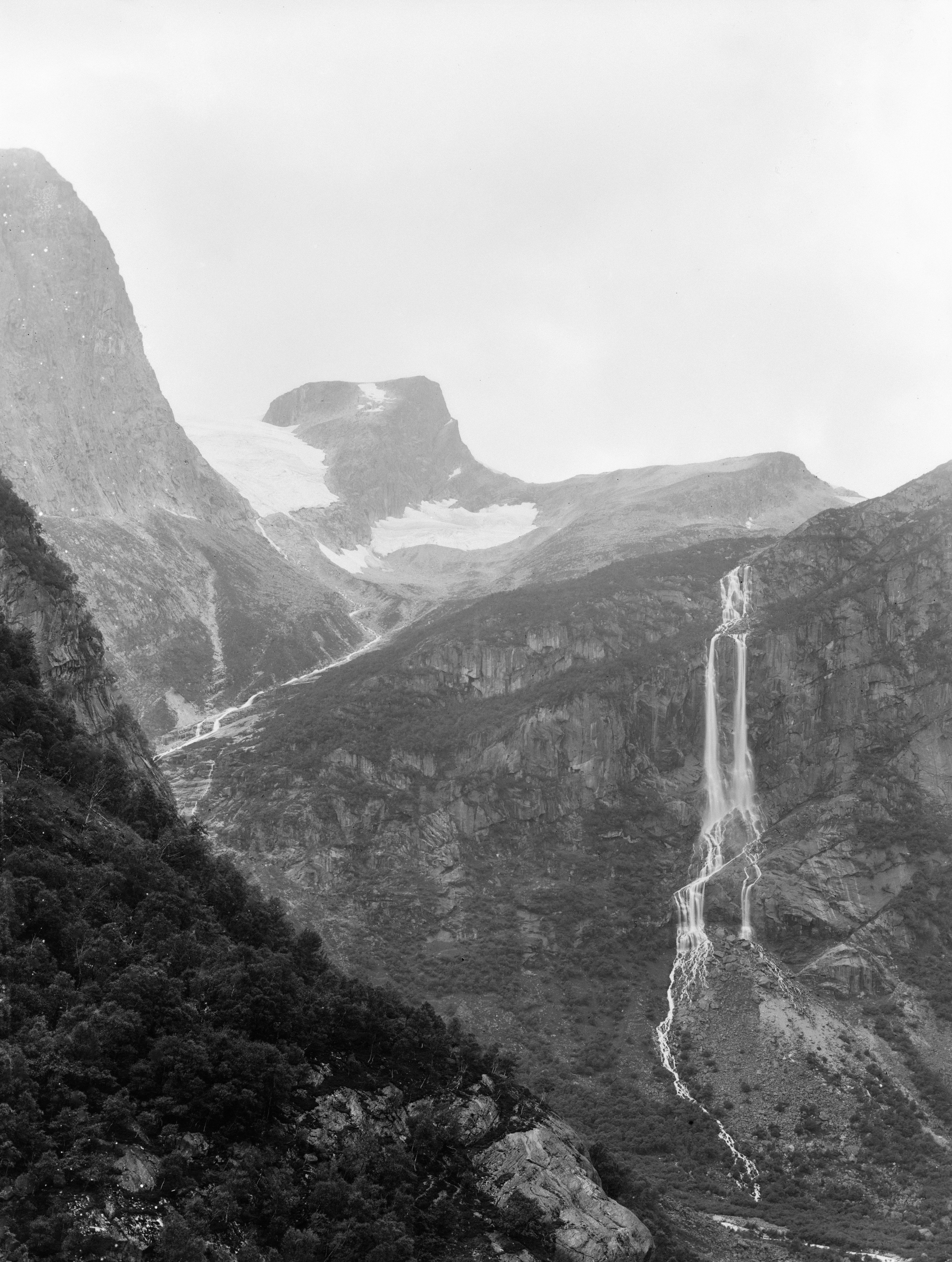 Black-and-white view of tall mountain cliffs with a long, narrow waterfall and glacier