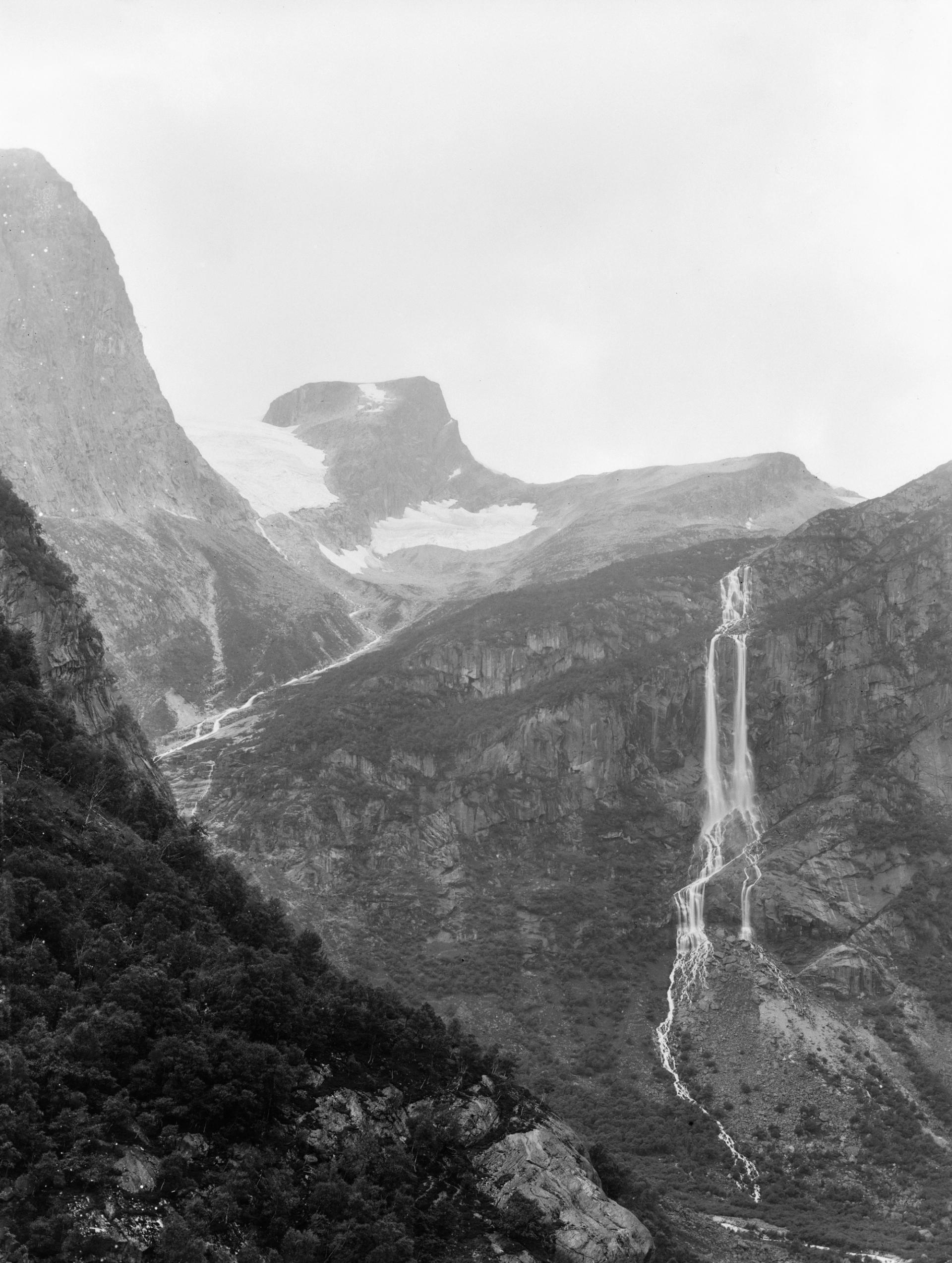 Black-and-white view of tall mountain cliffs with a long, narrow waterfall and glacier