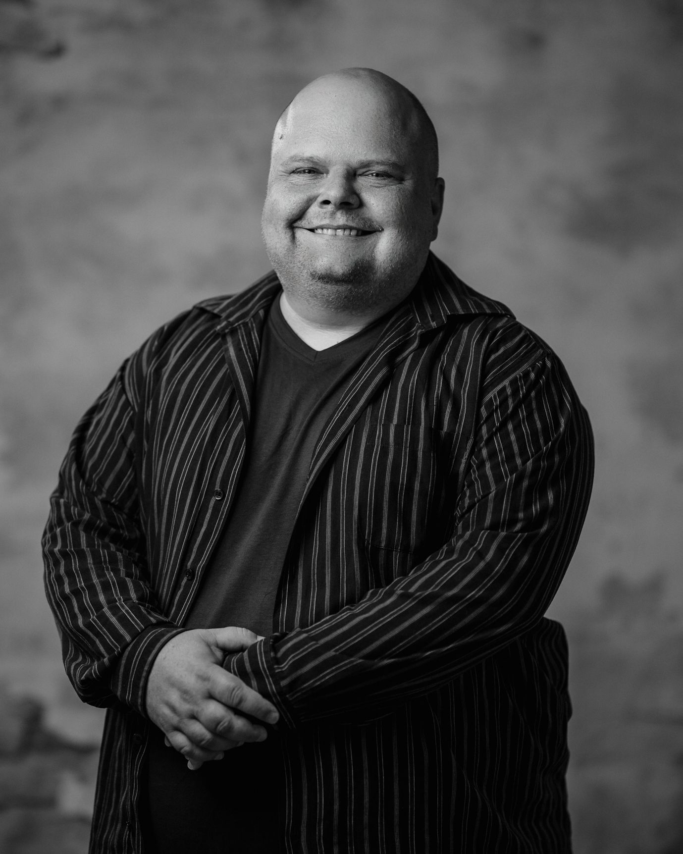 Smiling bald man in striped shirt posing against a plain studio backdrop