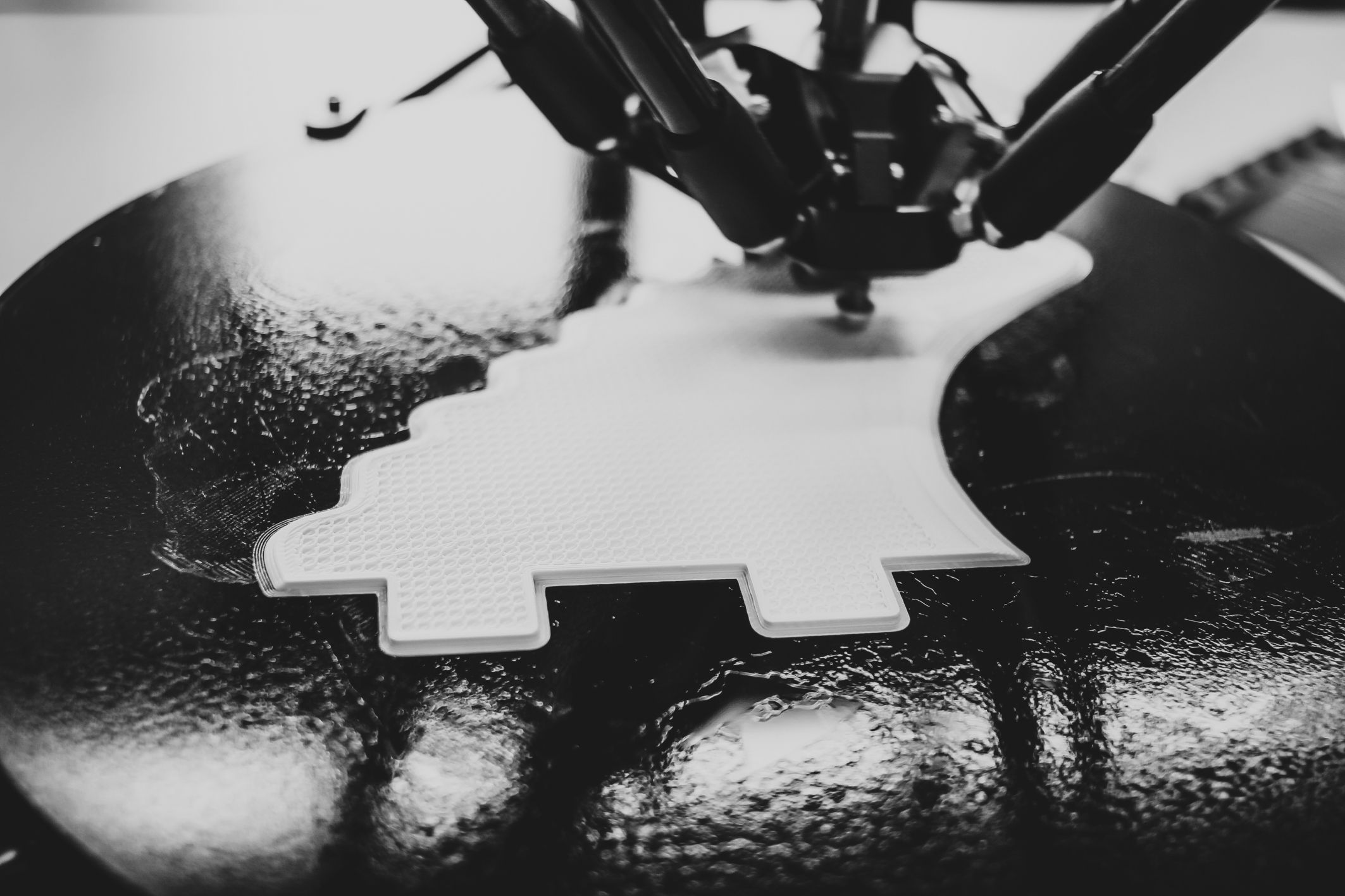 Close-up of a 3D printer nozzle creating a flat, pixelated white shape on the bed