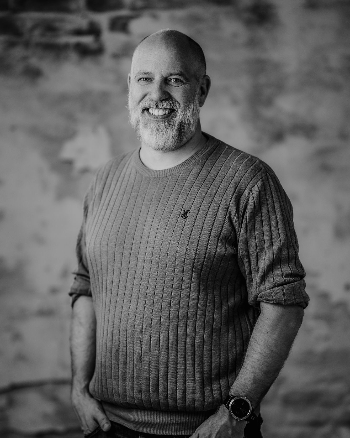 Smiling bearded man in a ribbed sweater poses against a blurred wall background