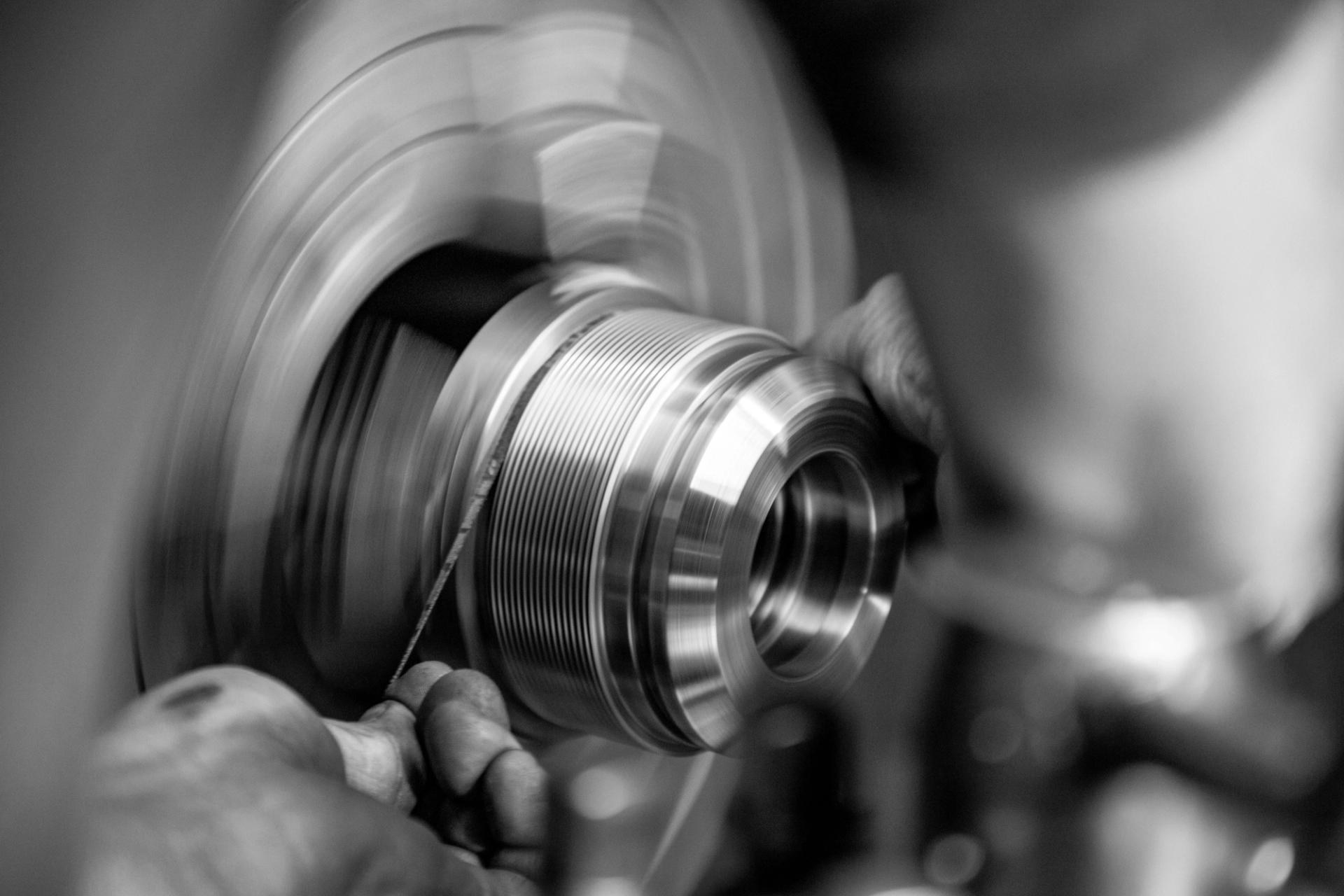 Worker’s hands machining a spinning metal part on a lathe in black and white.