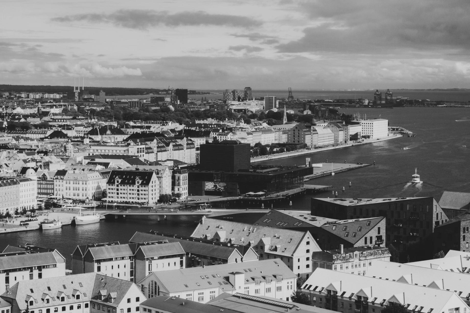 Black-and-white aerial view of a coastal city with dense buildings and a harbor