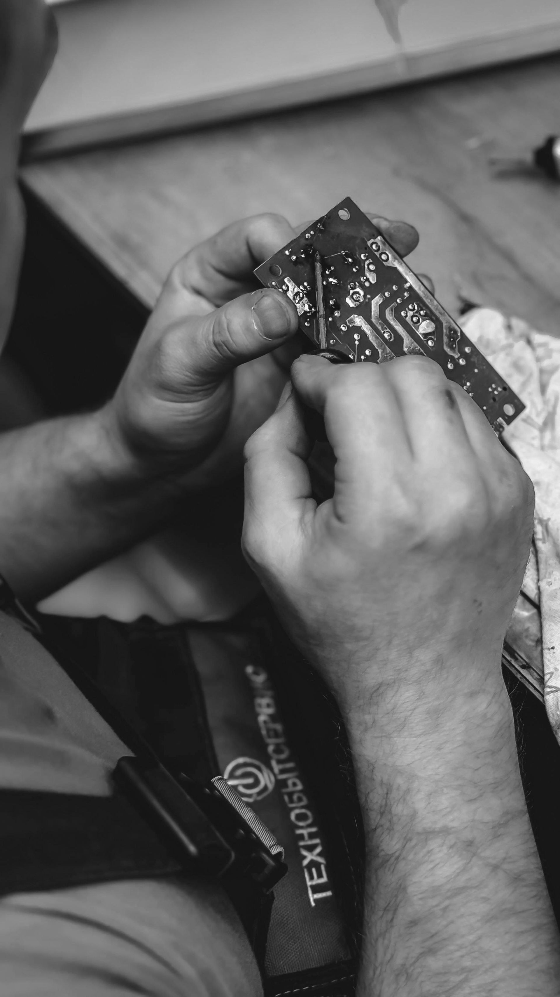Close-up of hands repairing a circuit board with a small tool.