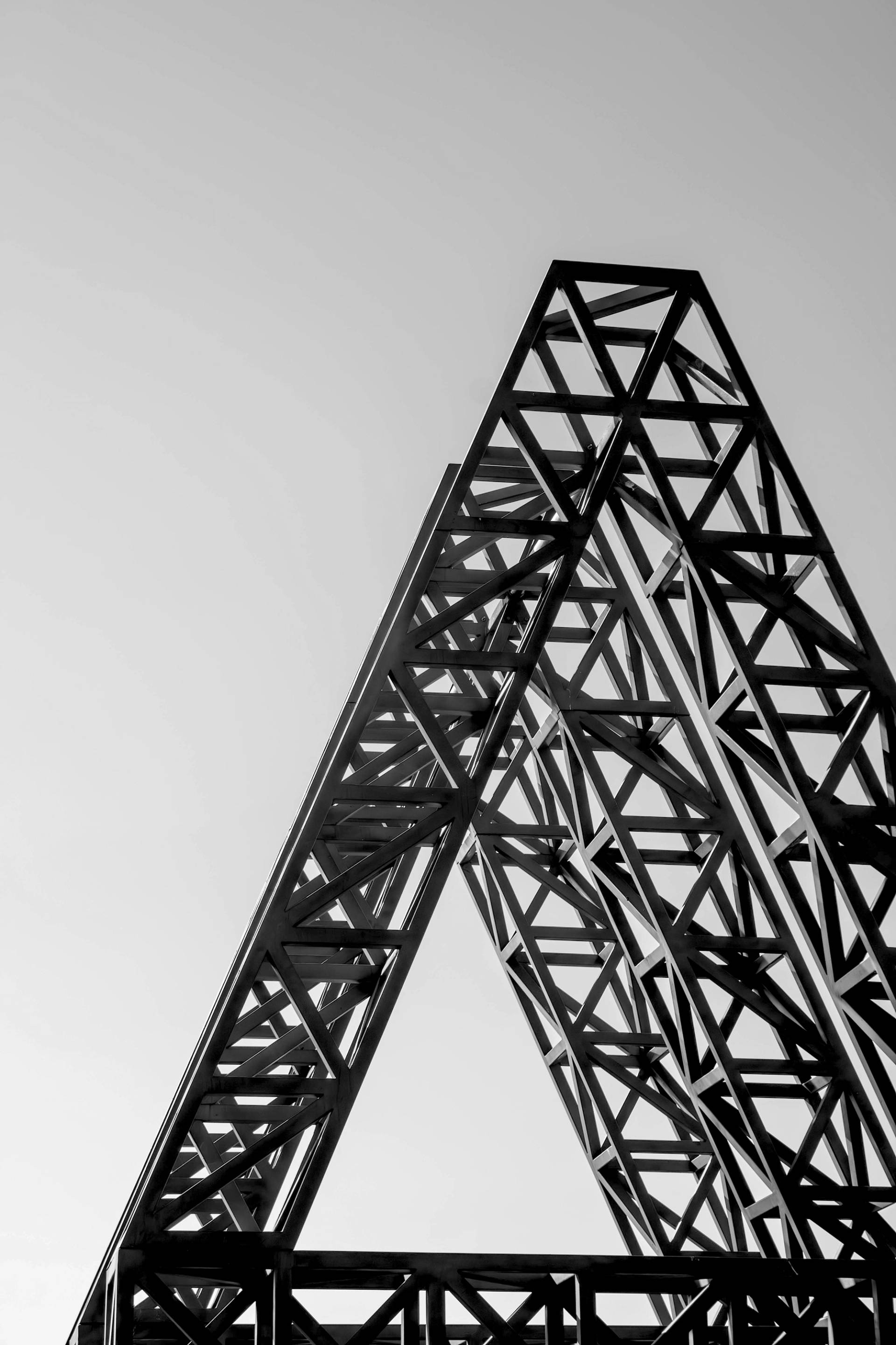 Black and white view of a triangular steel truss structure against the sky
