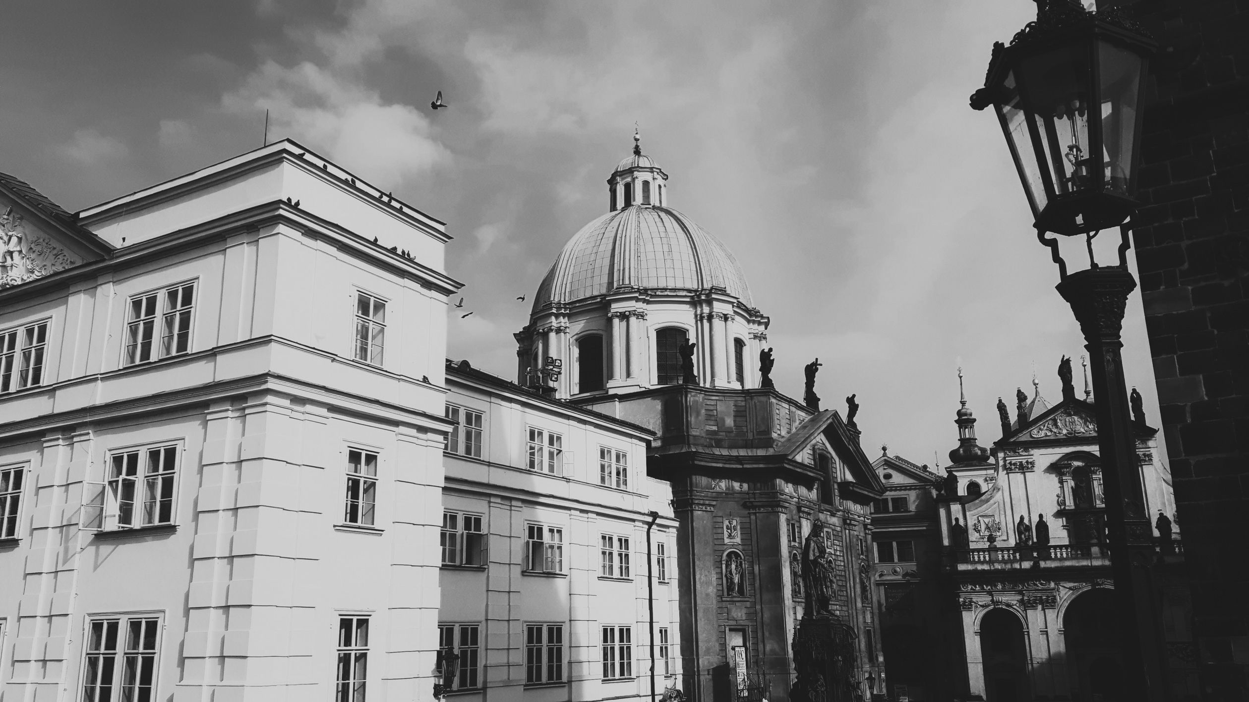 Black-and-white view of historic domed buildings with statues and a tall streetlamp