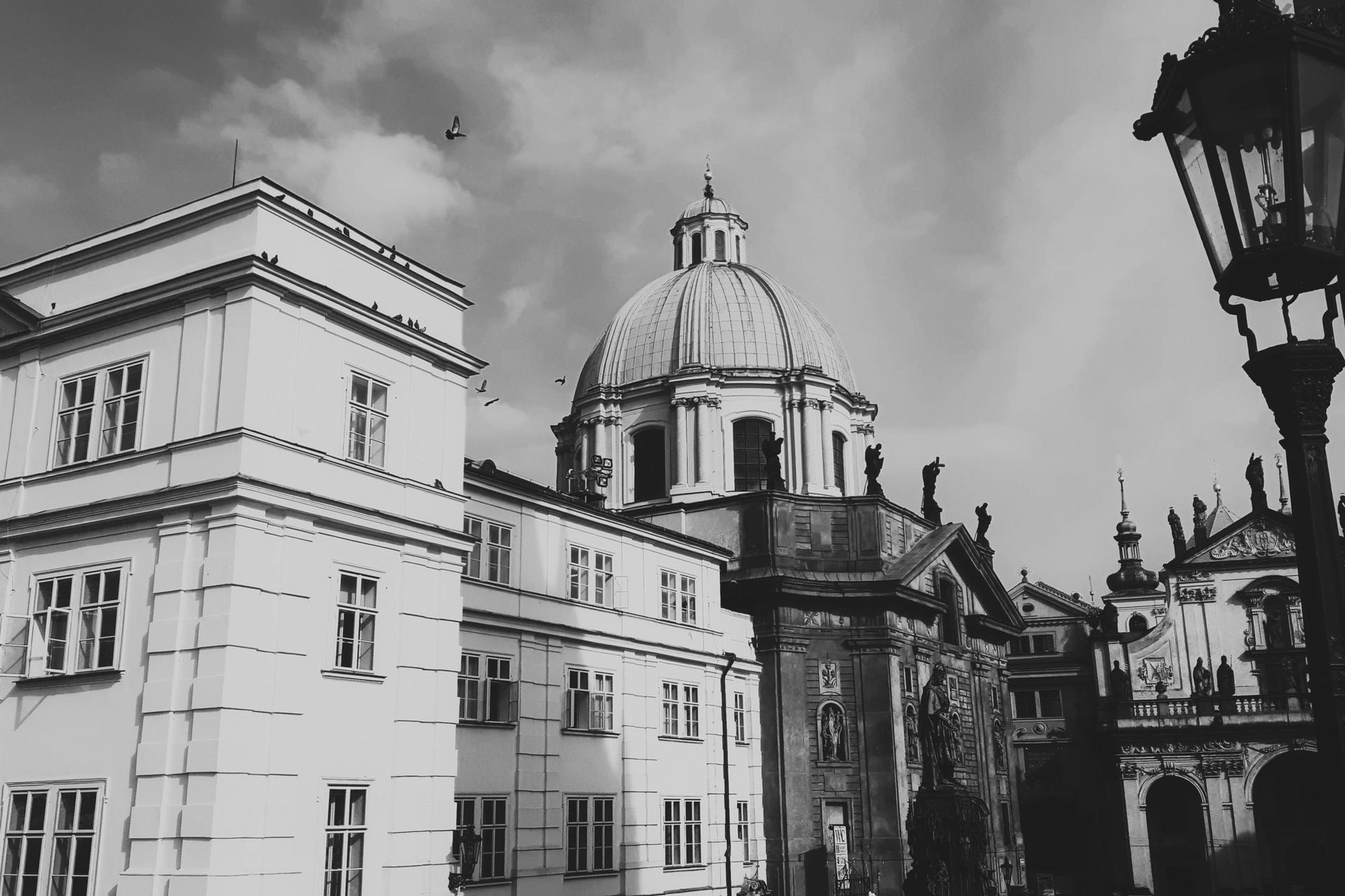 Black-and-white view of historic domed buildings with statues and a tall streetlamp