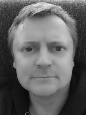 Black-and-white close-up of a person looking directly at the camera on a dark background