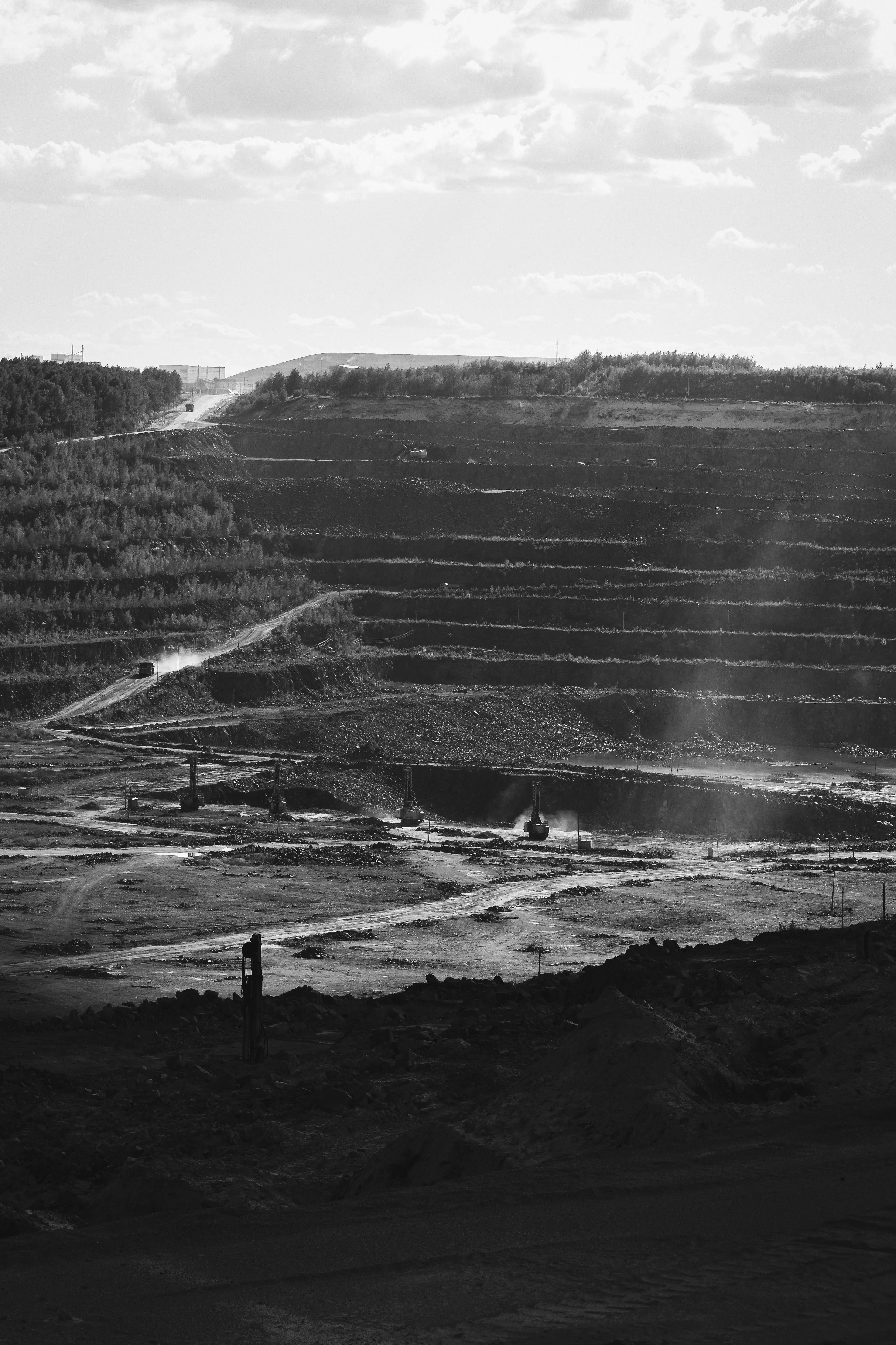 Black-and-white view of a vast terraced open-pit mine beneath a cloudy sky