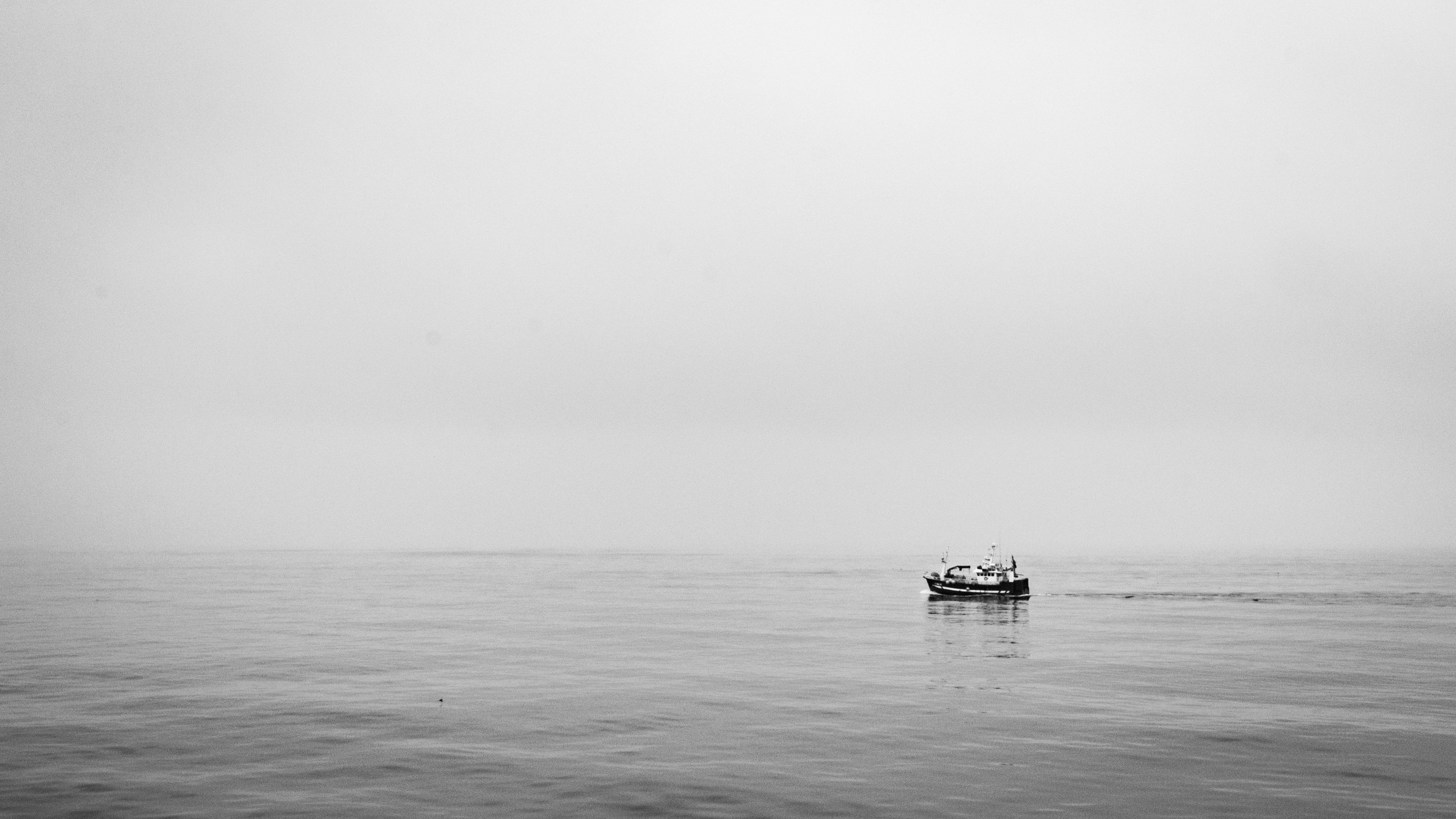 Small fishing boat alone on calm, foggy sea in black and white