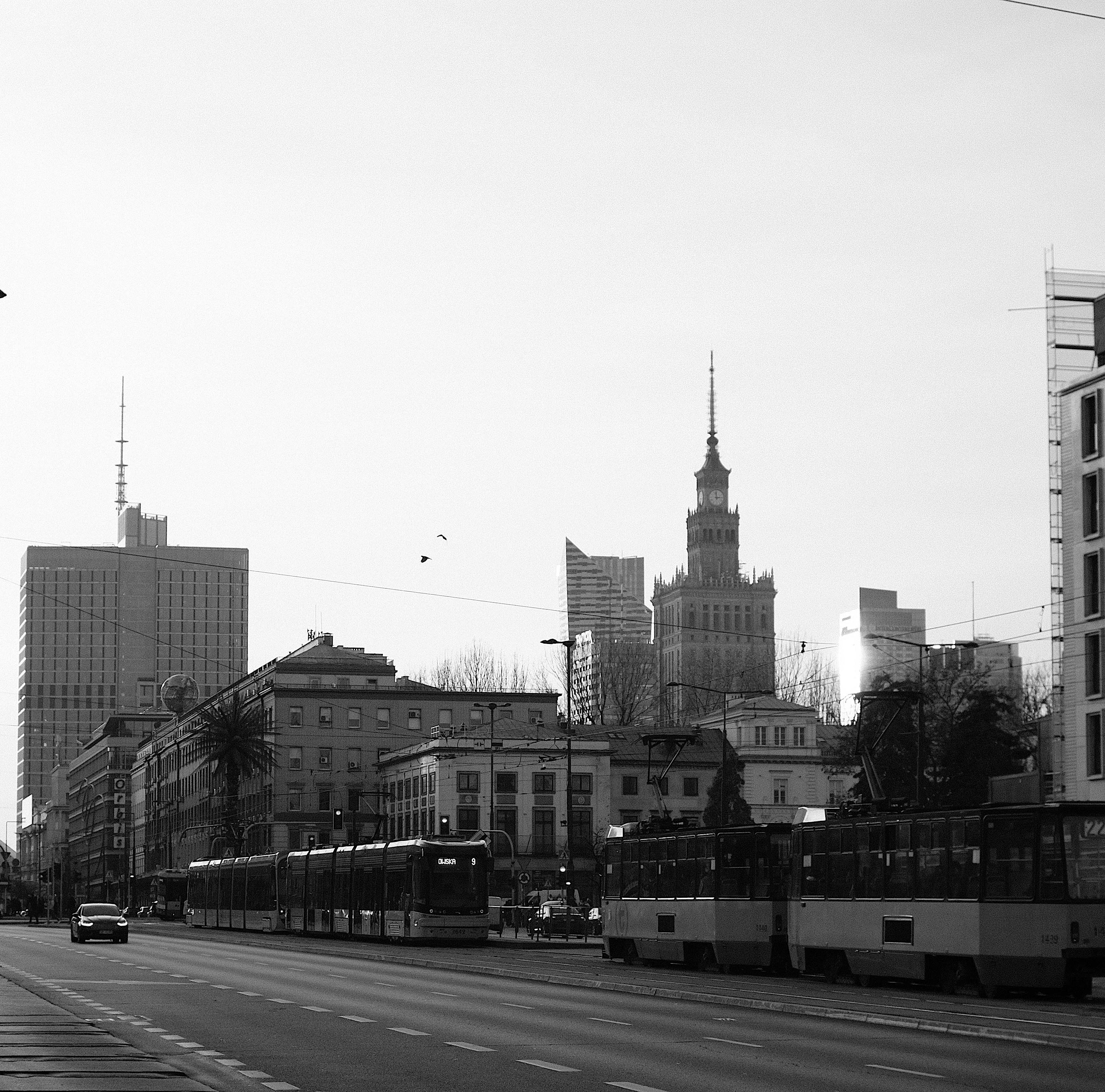Black-and-white city street with trams, cars, and tall buildings in the background