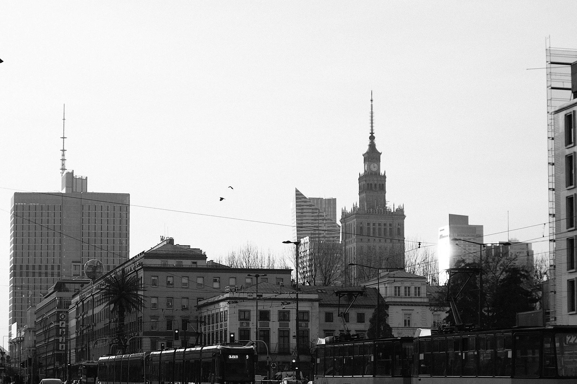 Black-and-white city street with trams, cars, and tall buildings in the background