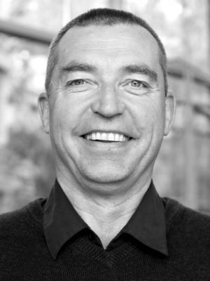 Black-and-white portrait of a smiling middle-aged man in a collared shirt and sweater