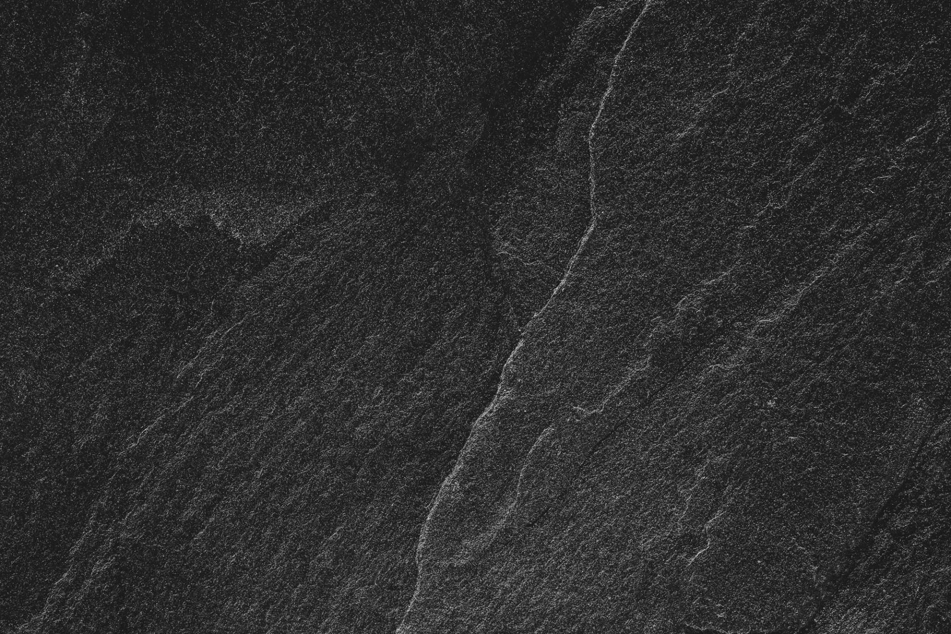 Close-up of dark textured stone surface with subtle gray veins and rough grain