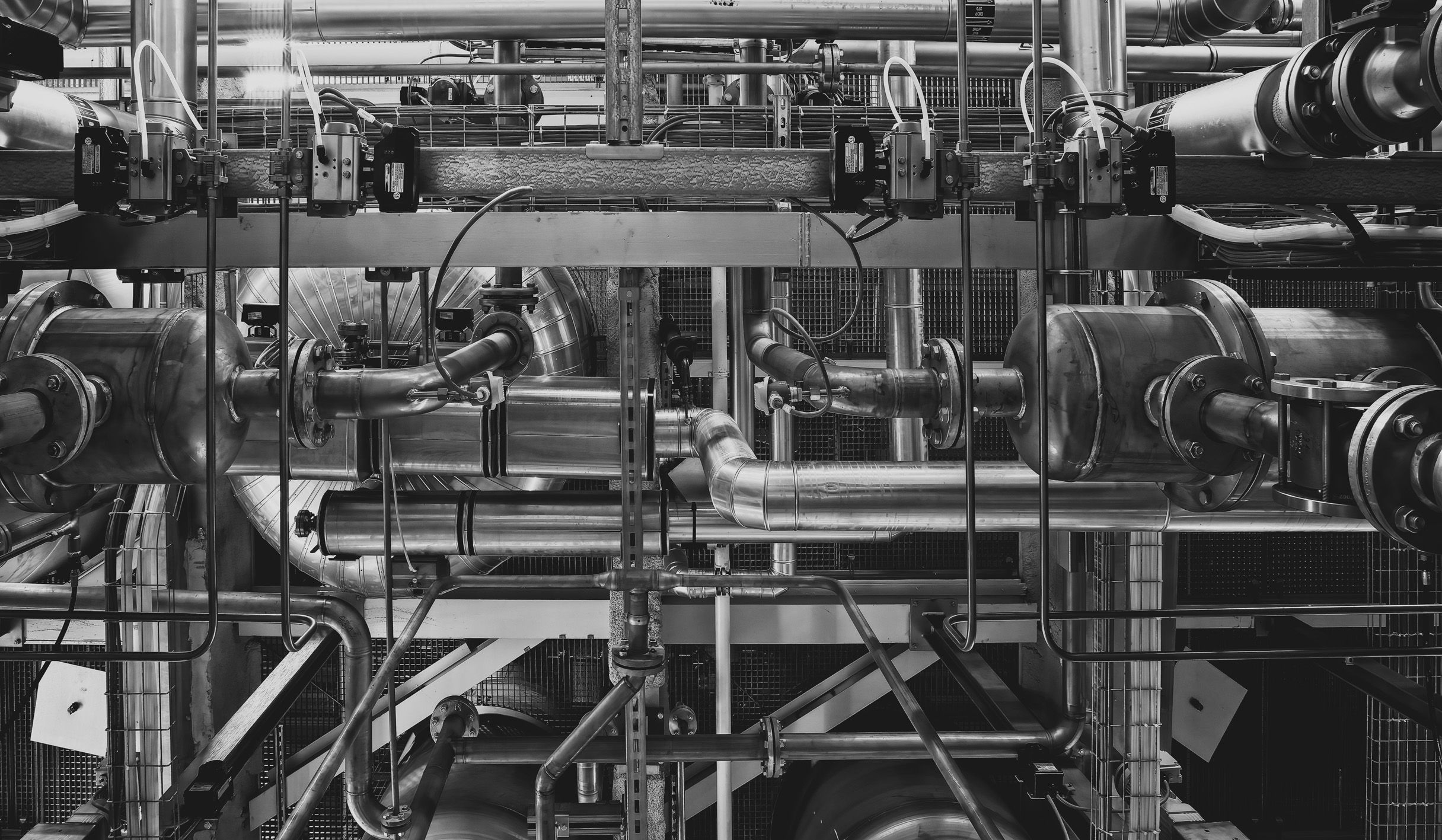 Black-and-white view of complex industrial metal pipes and machinery indoors