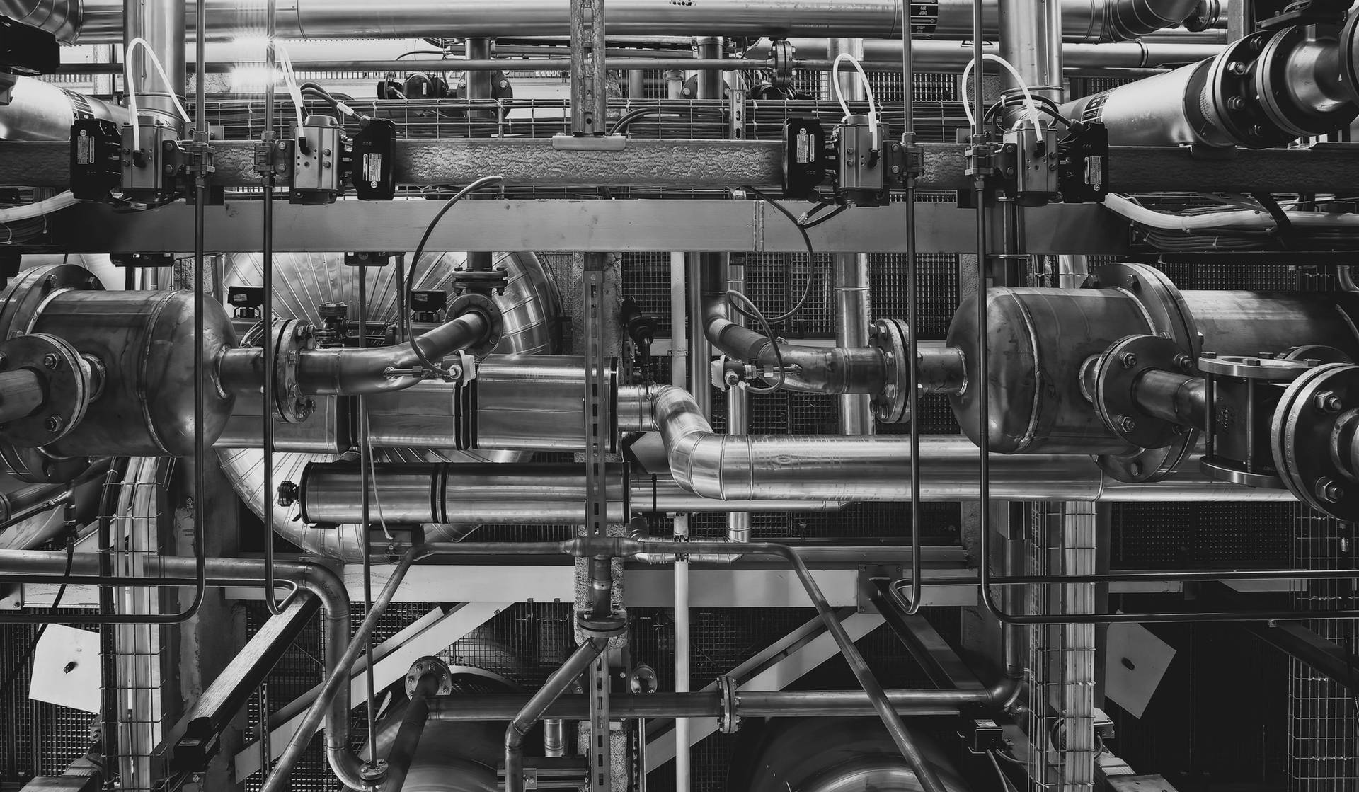 Black-and-white view of complex industrial metal pipes and machinery indoors